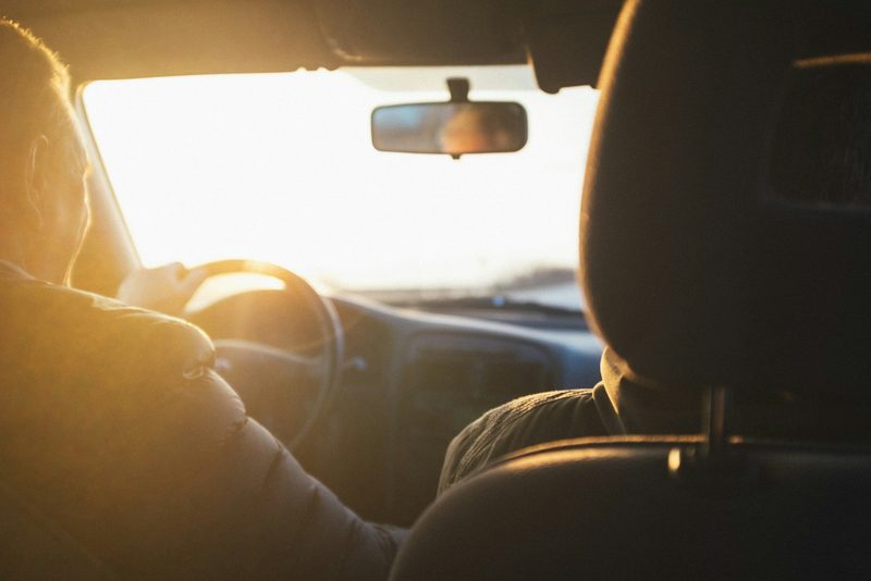 Eine Person fährt ein Auto bei Sonnenuntergang, die Sonne scheint durch die Windschutzscheibe.