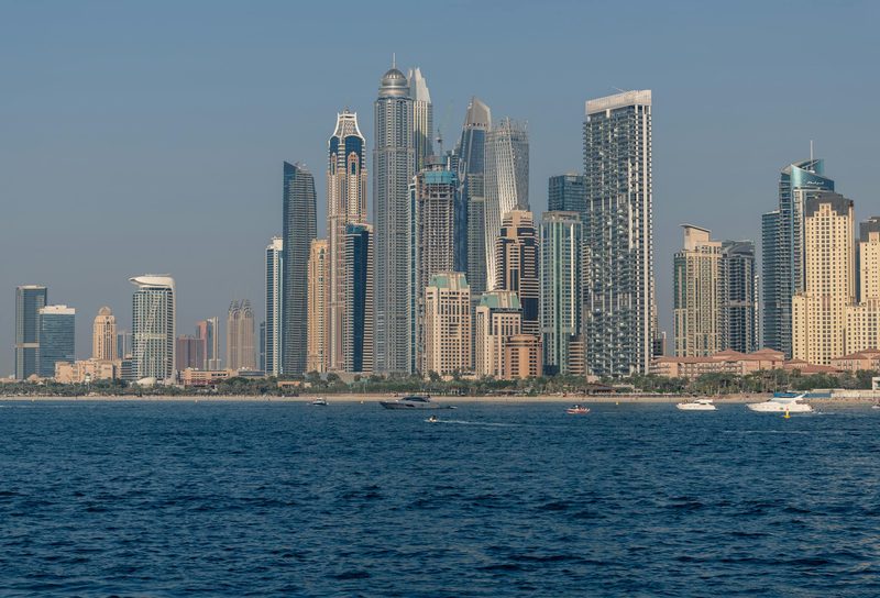 Arabische Emirate, Vereinigte Arabische Emirate - Eine Skyline mit vielen Hochhäusern und Wolkenkratzern am Meer, mit einem Strand und Booten im Vordergrund.