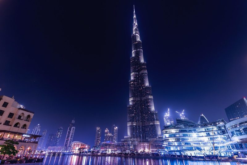 Arabische Emirate, Vereinigte Arabische Emirate - Der Burj Khalifa und umliegende Gebaeude in Dubai bei Nacht, beleuchtet und gespiegelt in einem Wasserbecken.
