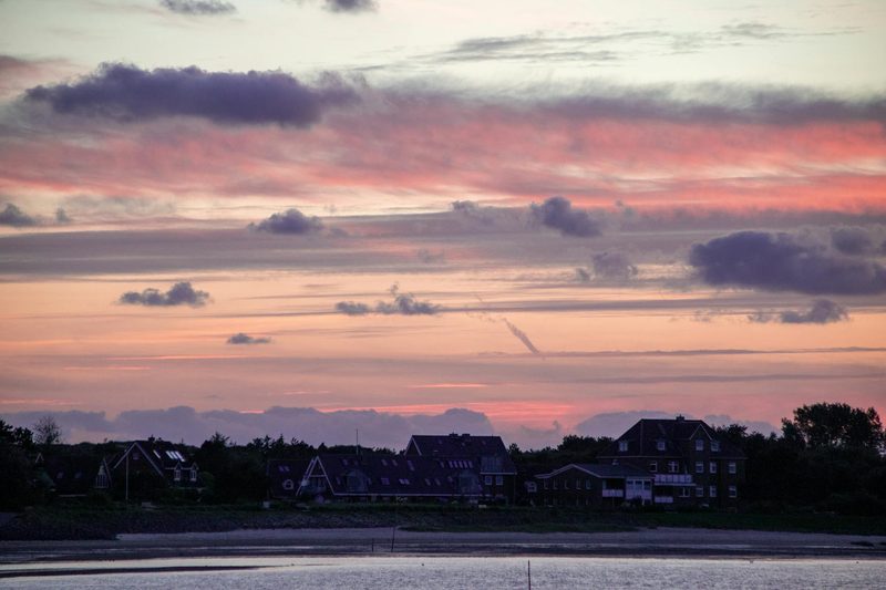 Haeuserfront eines Kuestenortes bei Sonnenuntergang mit rosa und violetten Wolken am Himmel.