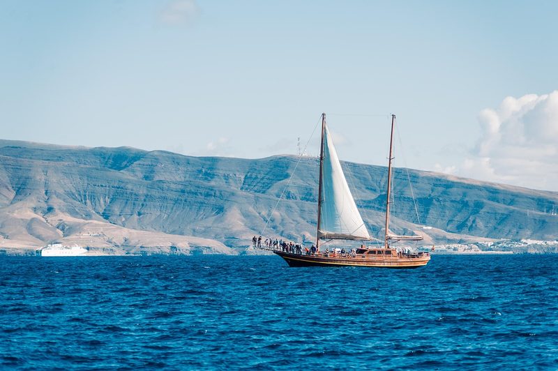 Ein Segelboot mit vielen Menschen an Bord fährt auf dem blauen Meer vor einer bergigen Küste.