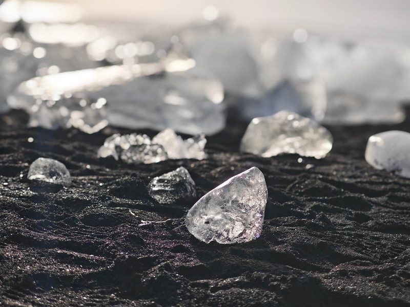 Eisbrocken liegen auf schwarzem Sand an einem Strand.