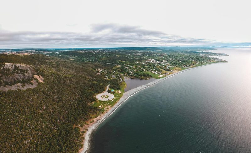 Luftaufnahme einer Stadt, die sich entlang einer felsigen Kueste erstreckt, mit einem dichten Wald auf der linken Seite und dem Meer auf der rechten Seite.