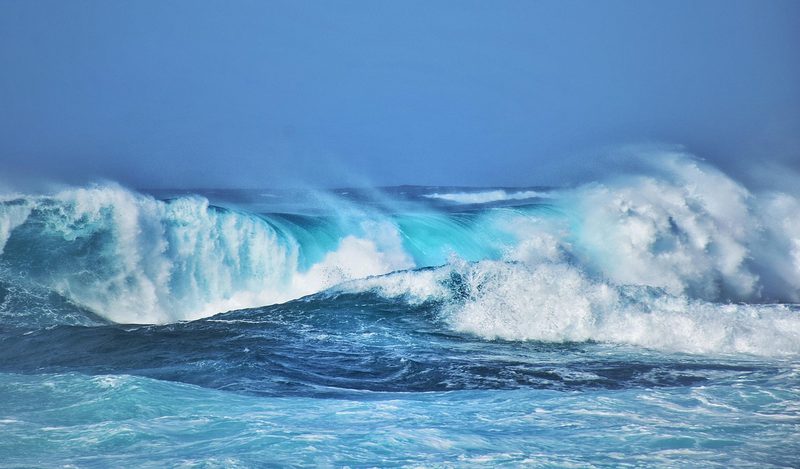 Eine grosse, brechende Welle im Meer unter einem blauen Himmel.