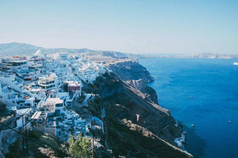 Eine weisse Stadt, die sich an eine steile Klippe ueber dem blauen Meer erstreckt.