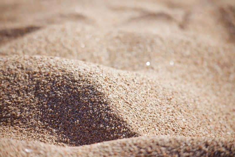 Nahaufnahme von Sand mit Wellenformen und Glitzerpartikeln.