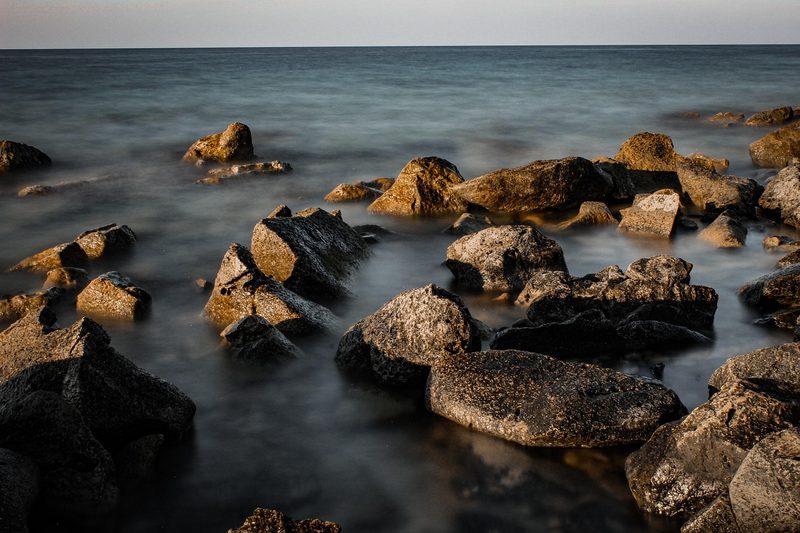 Felsen im Meer bei Sonnenuntergang mit leicht verschwommenem Wasser.