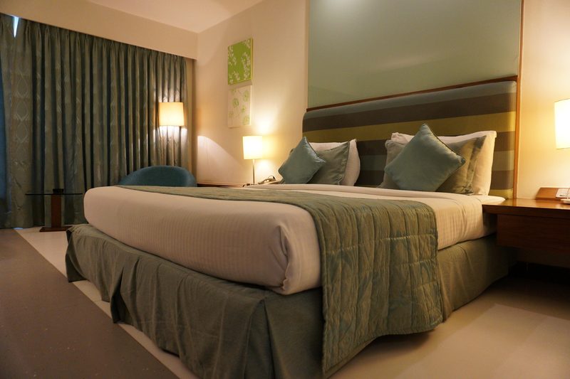 Ein Hotelzimmer mit einem großen Bett, das mit grünen und weißen Bettwäsche und Kissen dekoriert ist.
