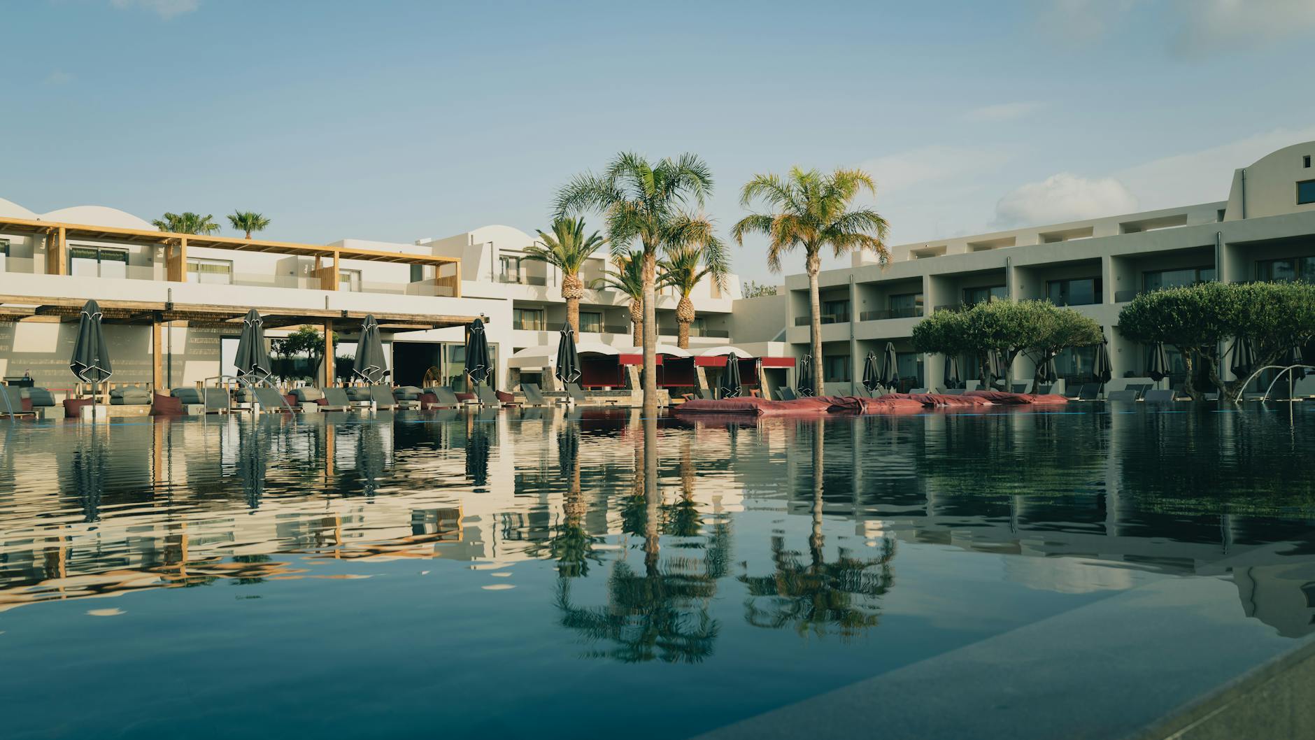 Hotel Resort Pool Luxus - Elegant resort with a pool and palm trees under a clear blue sky in Greece.