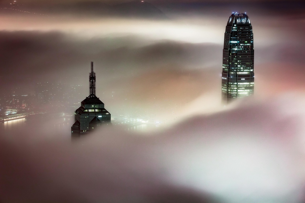 Zwei Wolkenkratzer ragen aus dichtem Nebel hervor, beleuchtet von den Lichtern der Stadt bei Nacht.