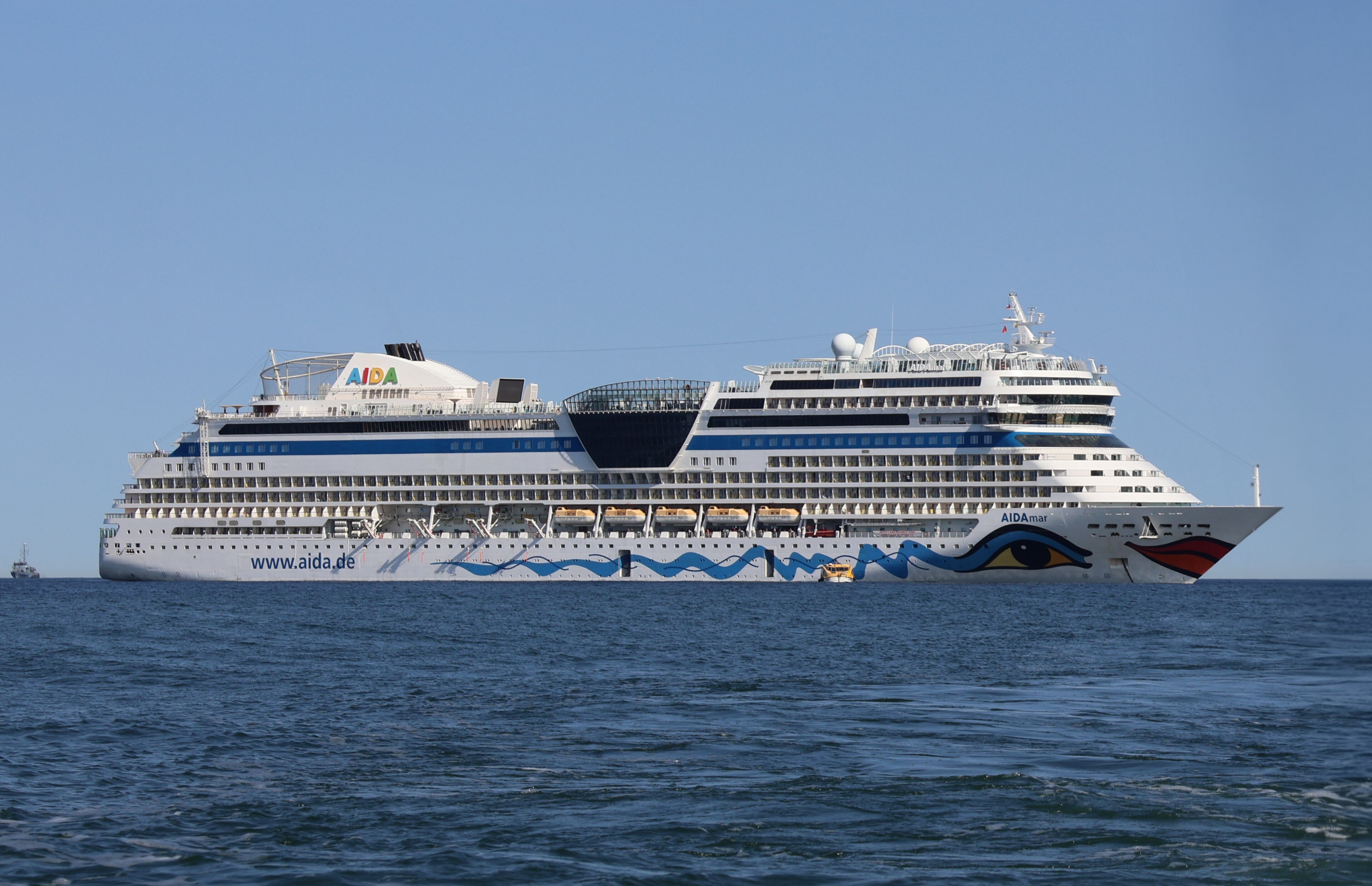 Ein großes weißes Kreuzfahrtschiff mit dem Namen AIDAmare und der Aufschrift www.aida.de auf dem Meer vor einem blauen Himmel.