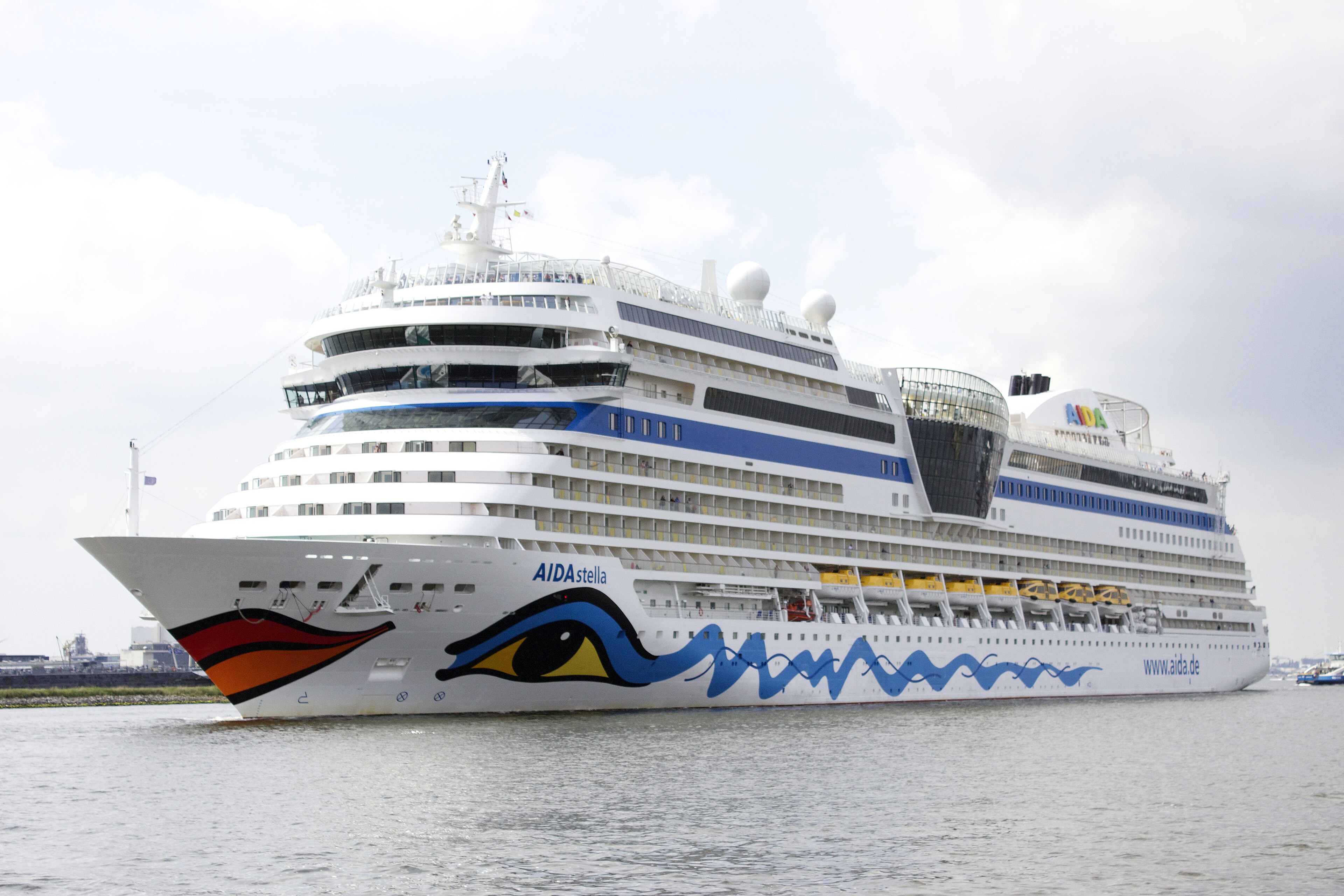Ein großes weißes Kreuzfahrtschiff mit dem Namen AIDAstella und einem bunten Auge auf der Seite fährt auf dem Wasser.