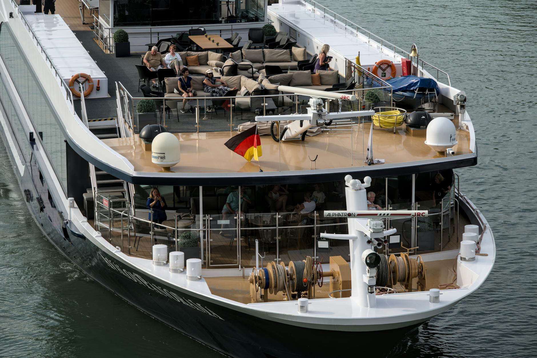 Ein Flusskreuzfahrtschiff mit Passagieren auf dem Sonnendeck und der deutschen Flagge, die im Wind weht.