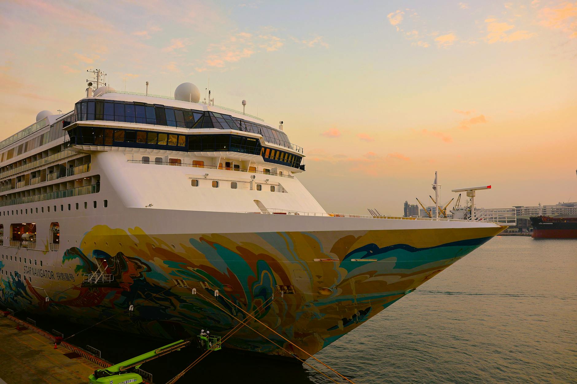 Ein großes Kreuzfahrtschiff mit einer bunten Bemalung am Bug liegt im Hafen bei Sonnenuntergang vor Anker.