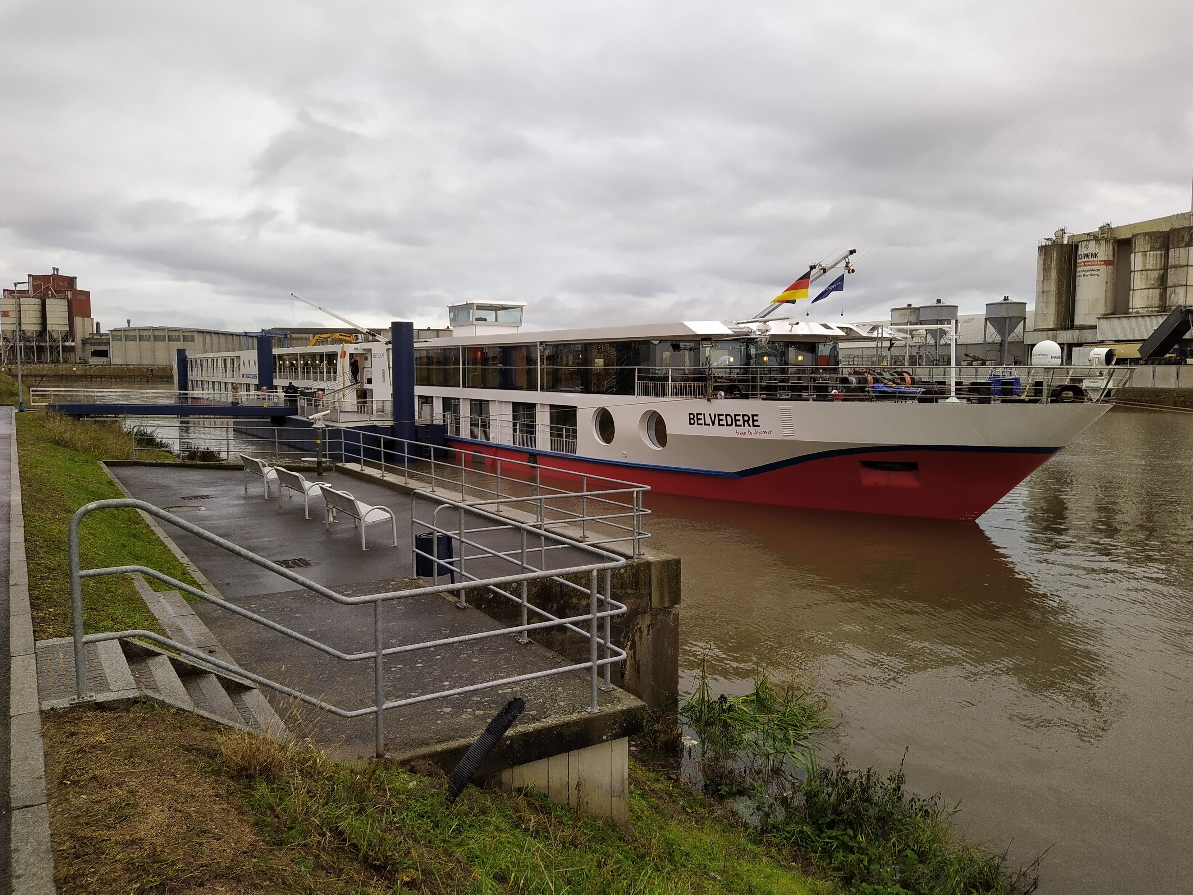 Ein Flusskreuzfahrtschiff namens Belvedere liegt im Hafen neben Industriegebäuden.