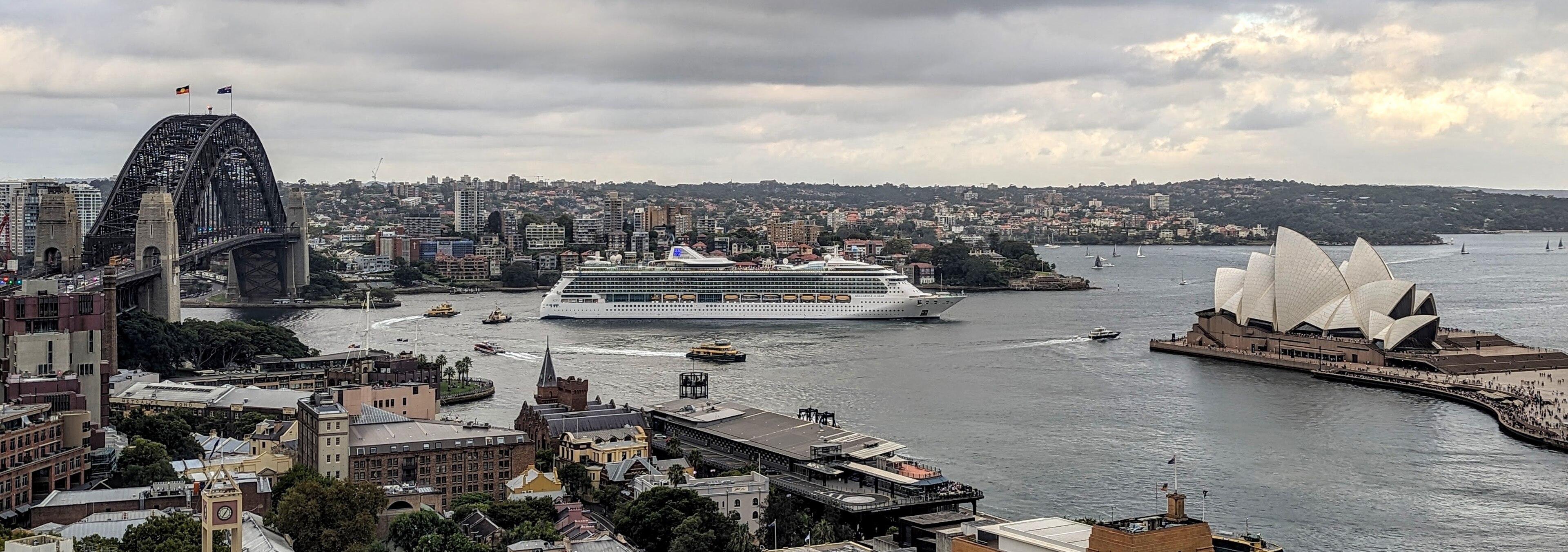 Ein Kreuzfahrtschiff fährt im Hafen von Sydney an der Oper und der Harbour Bridge vorbei.