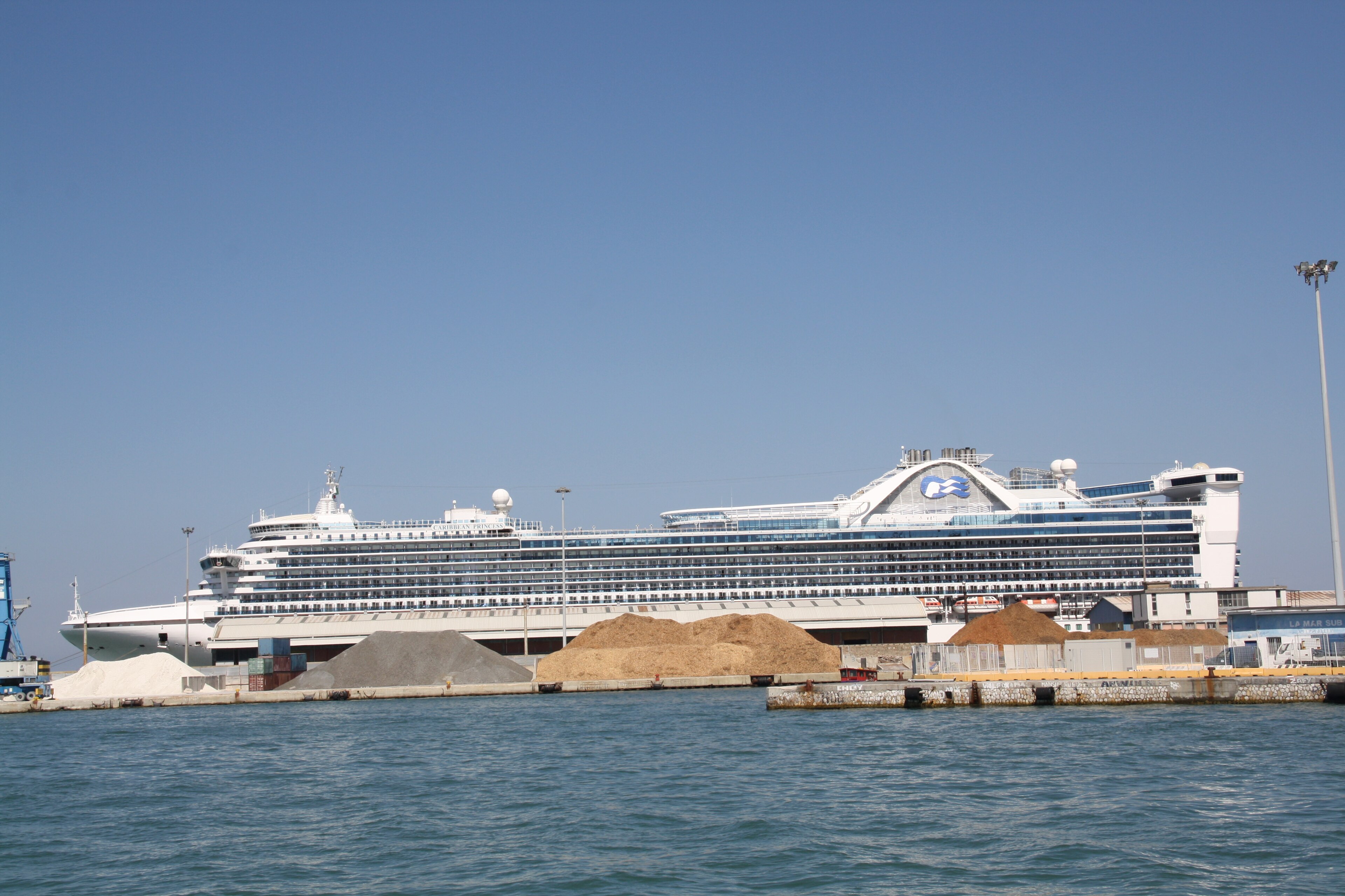 Ein großes weißes Kreuzfahrtschiff liegt im Hafen vor einer blauen Kulisse.