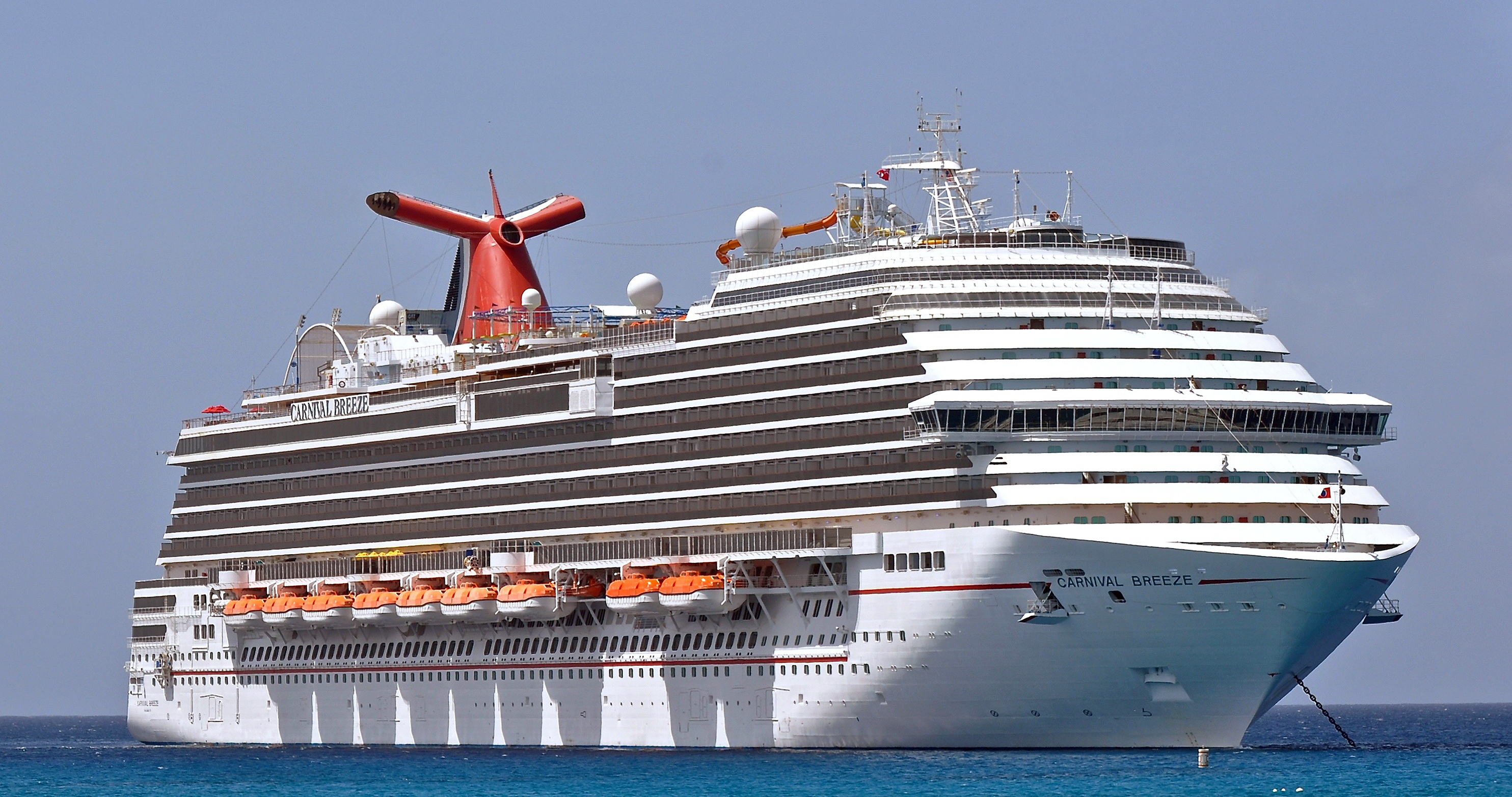Ein großes weißes Kreuzfahrtschiff mit dem Namen Carnival Breeze liegt im blauen Wasser.