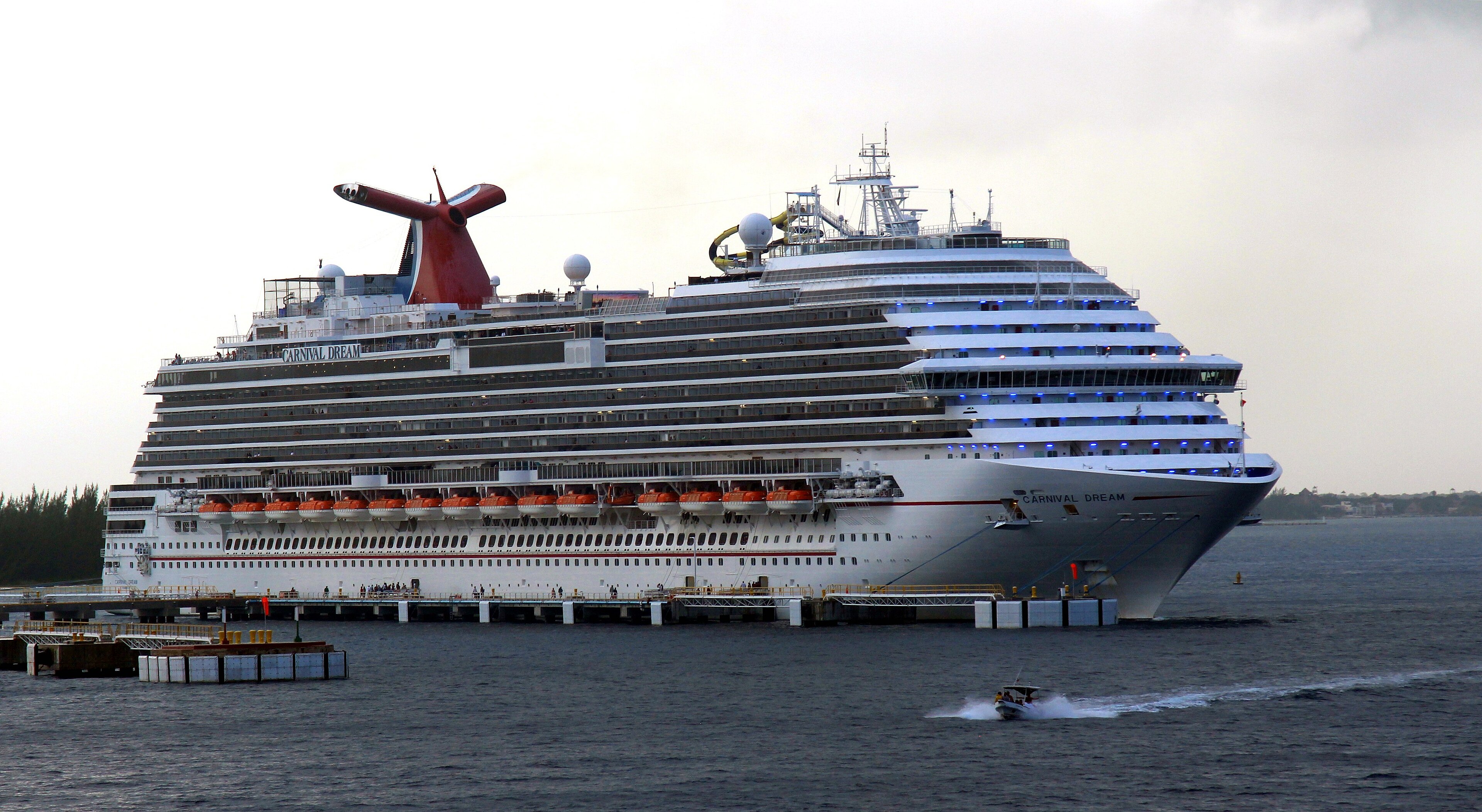 Ein großes Kreuzfahrtschiff namens Carnival Dream liegt an einem Pier im Wasser, während ein kleines Boot vorbeifährt.