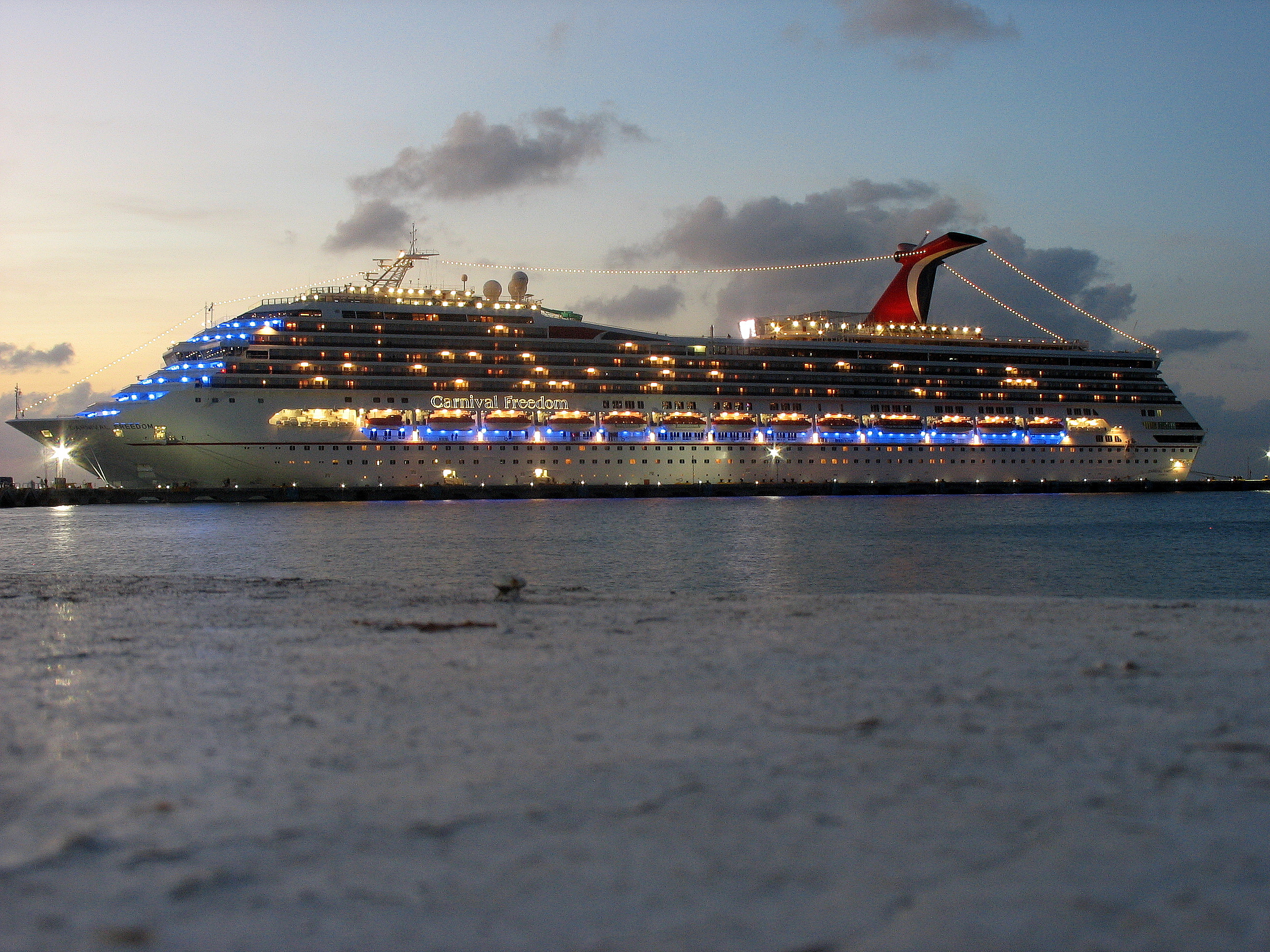 Ein großes Kreuzfahrtschiff namens Carnival Freedom liegt im Hafen, beleuchtet bei Dämmerung.