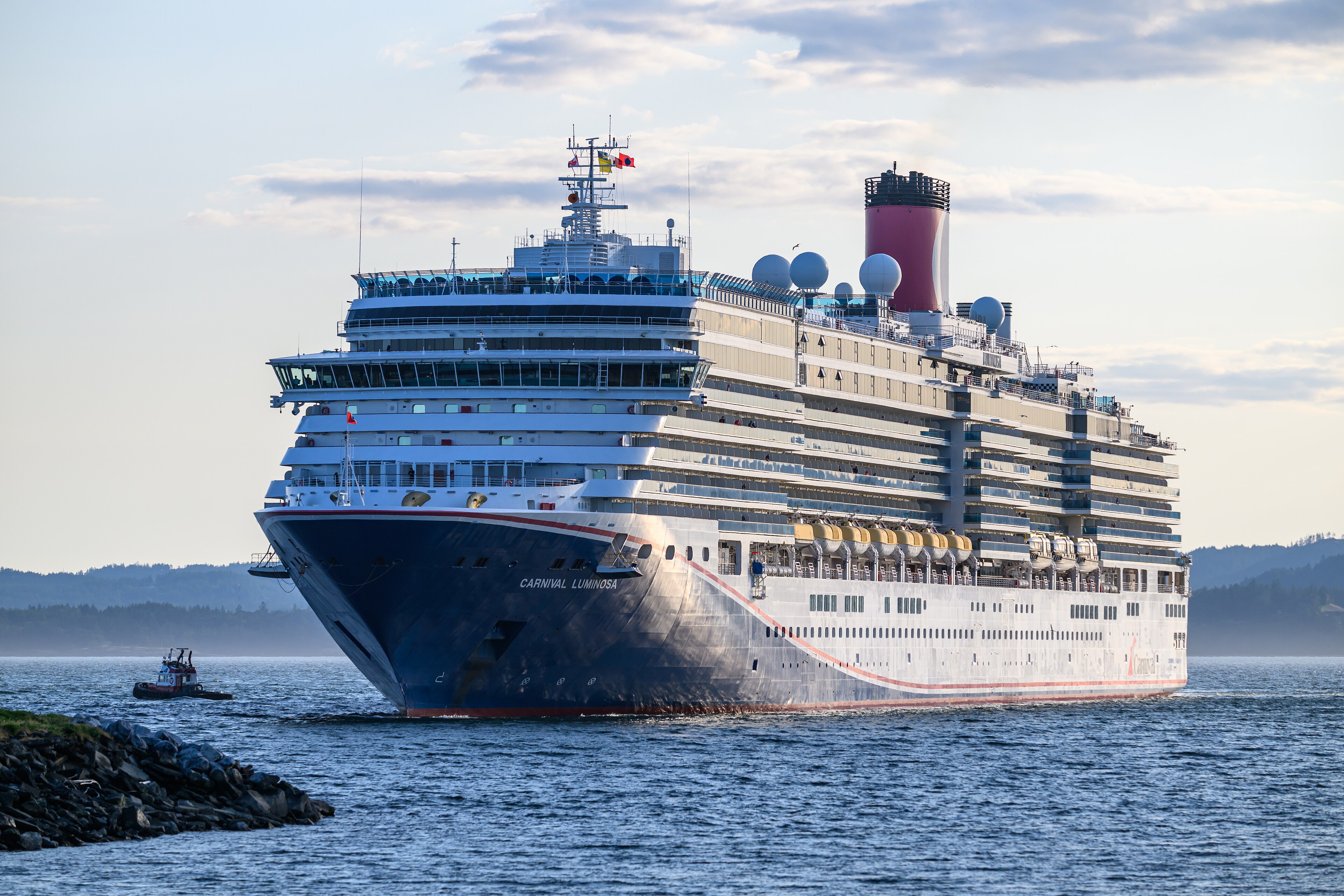 Ein großes Kreuzfahrtschiff namens Carnival Luminosa fährt auf dem Meer, begleitet von einem Schlepper.