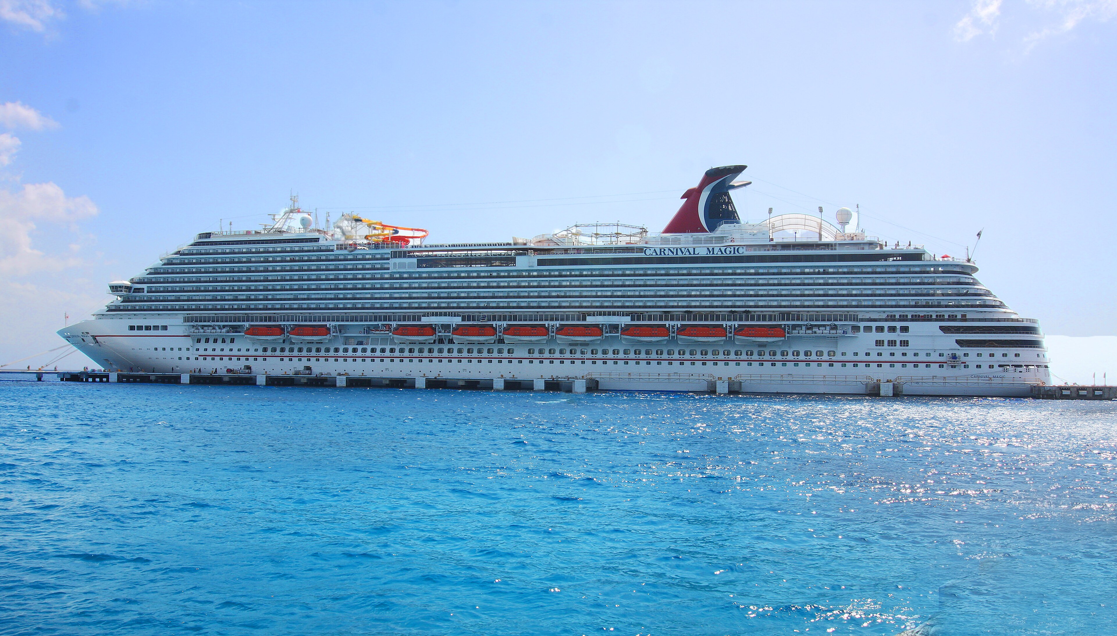 Ein großes weißes Kreuzfahrtschiff namens Carnival Magic liegt an einem Pier im blauen Meer.