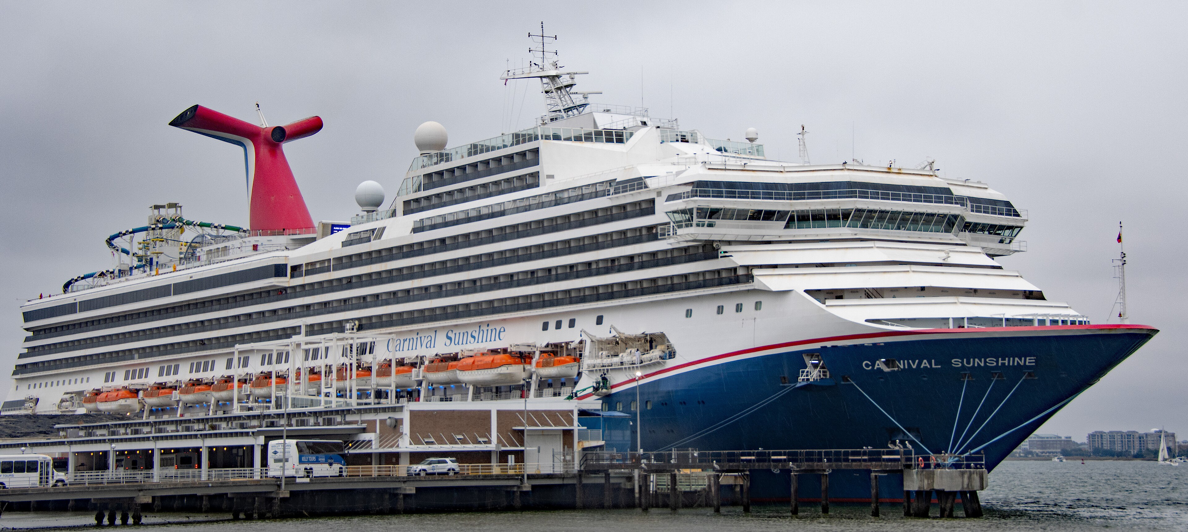 Das Kreuzfahrtschiff Carnival Sunshine liegt an einem Pier, mit Rettungsbooten an der Seite und einer Wasserrutsche auf dem Oberdeck.