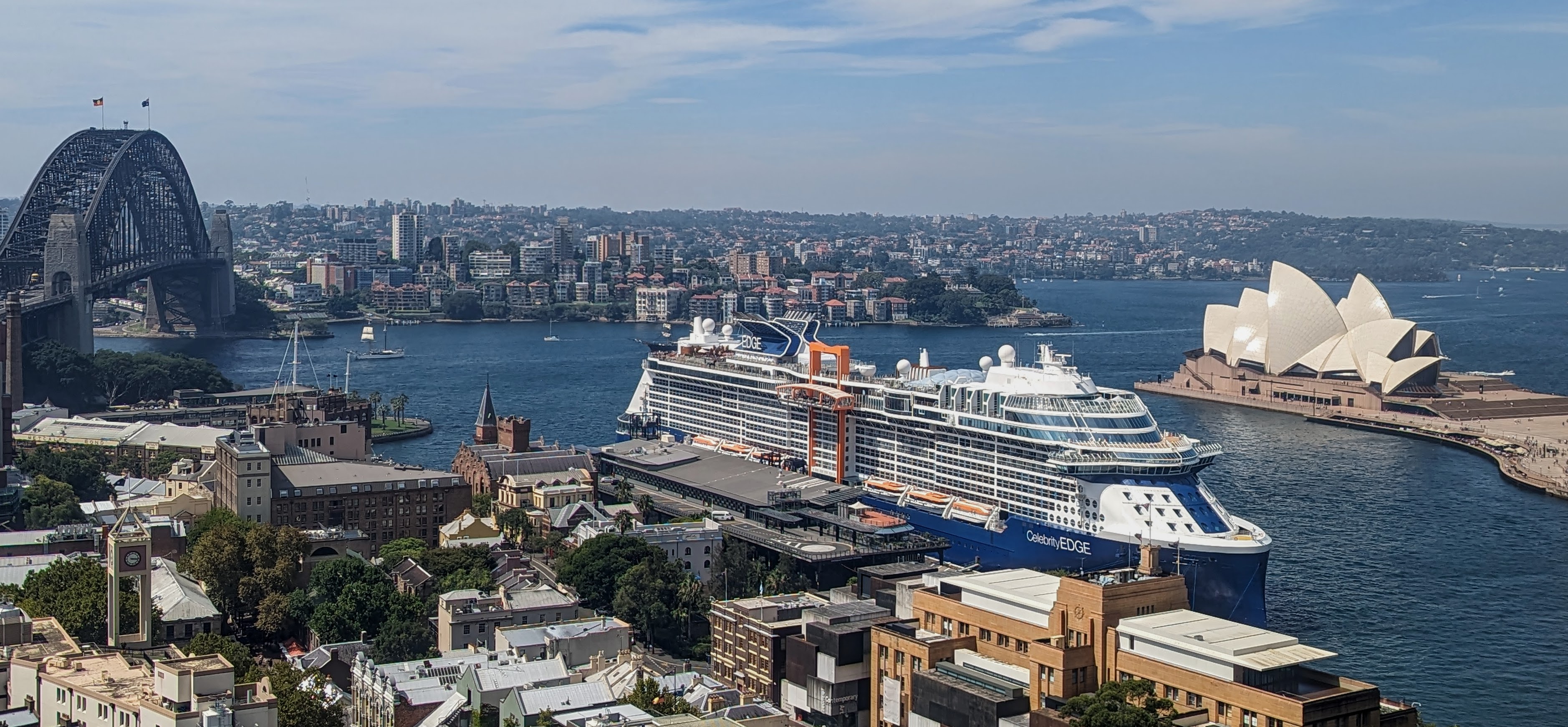 Ein Kreuzfahrtschiff liegt im Hafen von Sydney neben der Sydney Harbour Bridge und dem Sydney Opera House.