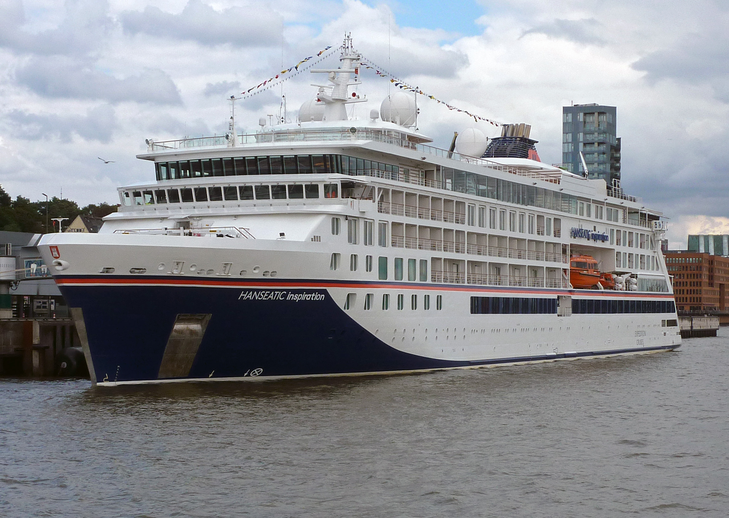 Ein großes weißes Kreuzfahrtschiff mit dem Namen HANSEATIC Inspiration auf dem Rumpf fährt auf dem Wasser.