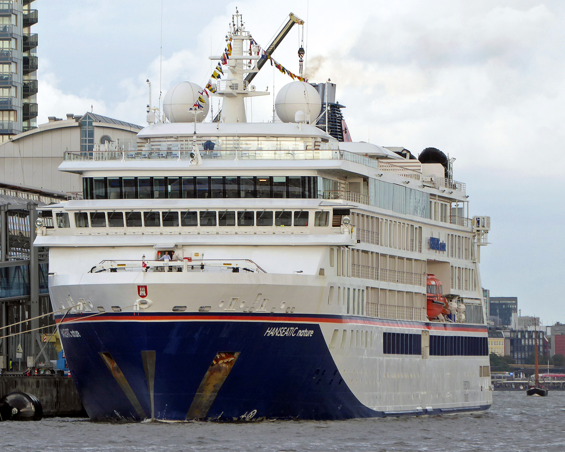 Ein großes weißes Kreuzfahrtschiff mit dem Namen HANSEATIC nature liegt im Hafen vor Anker.