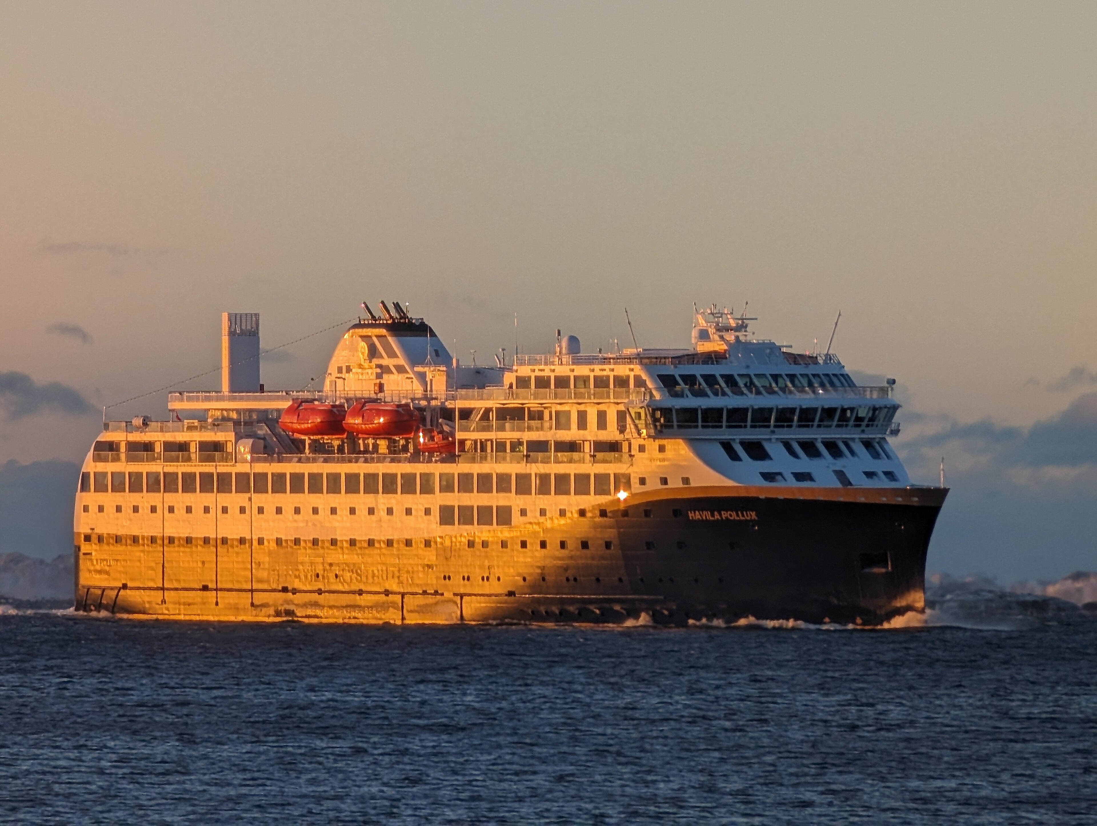 Ein großes Passagierschiff mit dem Namen Havila Pollux fährt auf dem Meer, beleuchtet von der tiefstehenden Sonne.