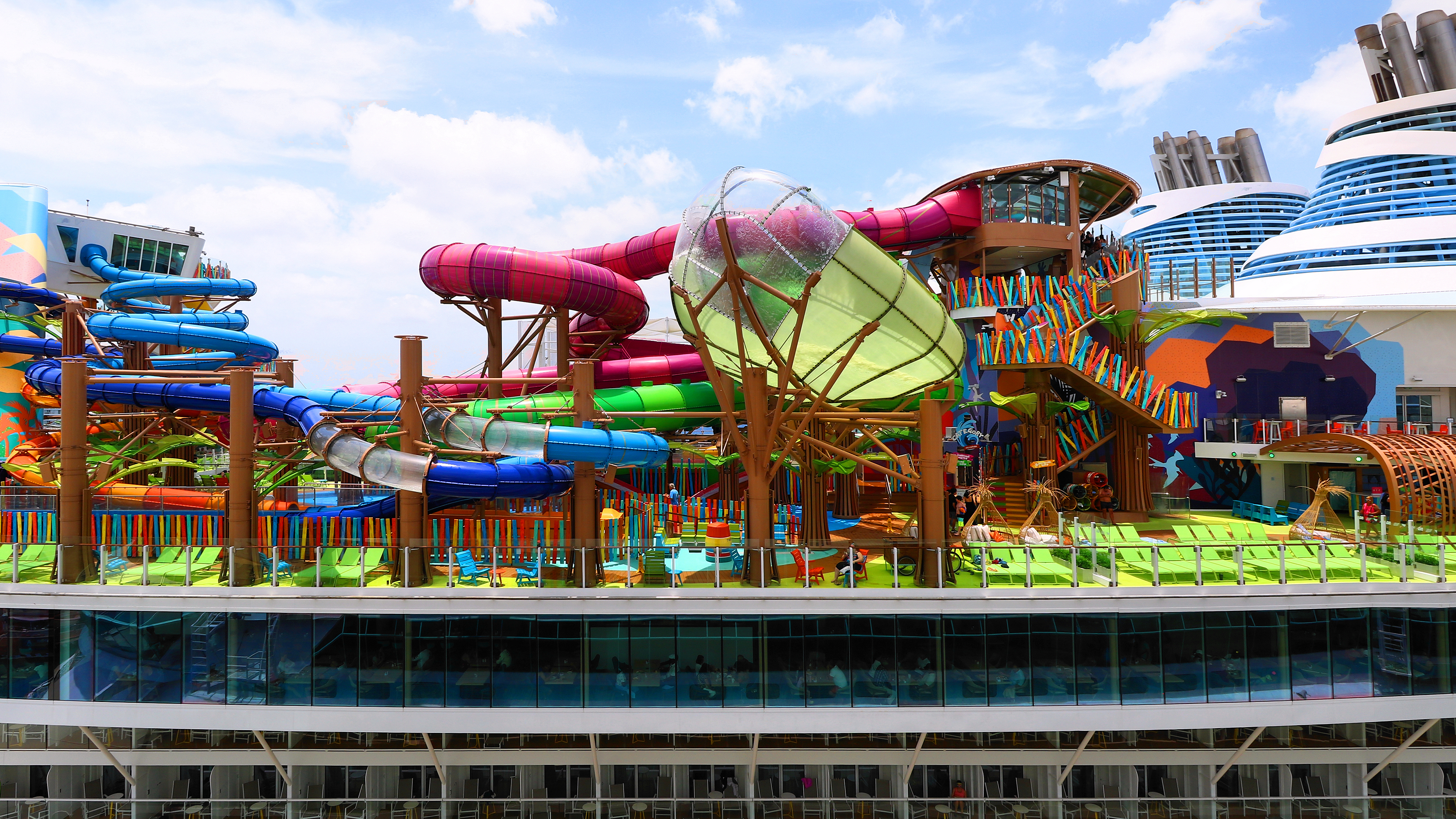 Ein Kreuzfahrtschiff mit einem großen Wasserpark auf dem Oberdeck, inklusive bunter Wasserrutschen und Liegestühlen.