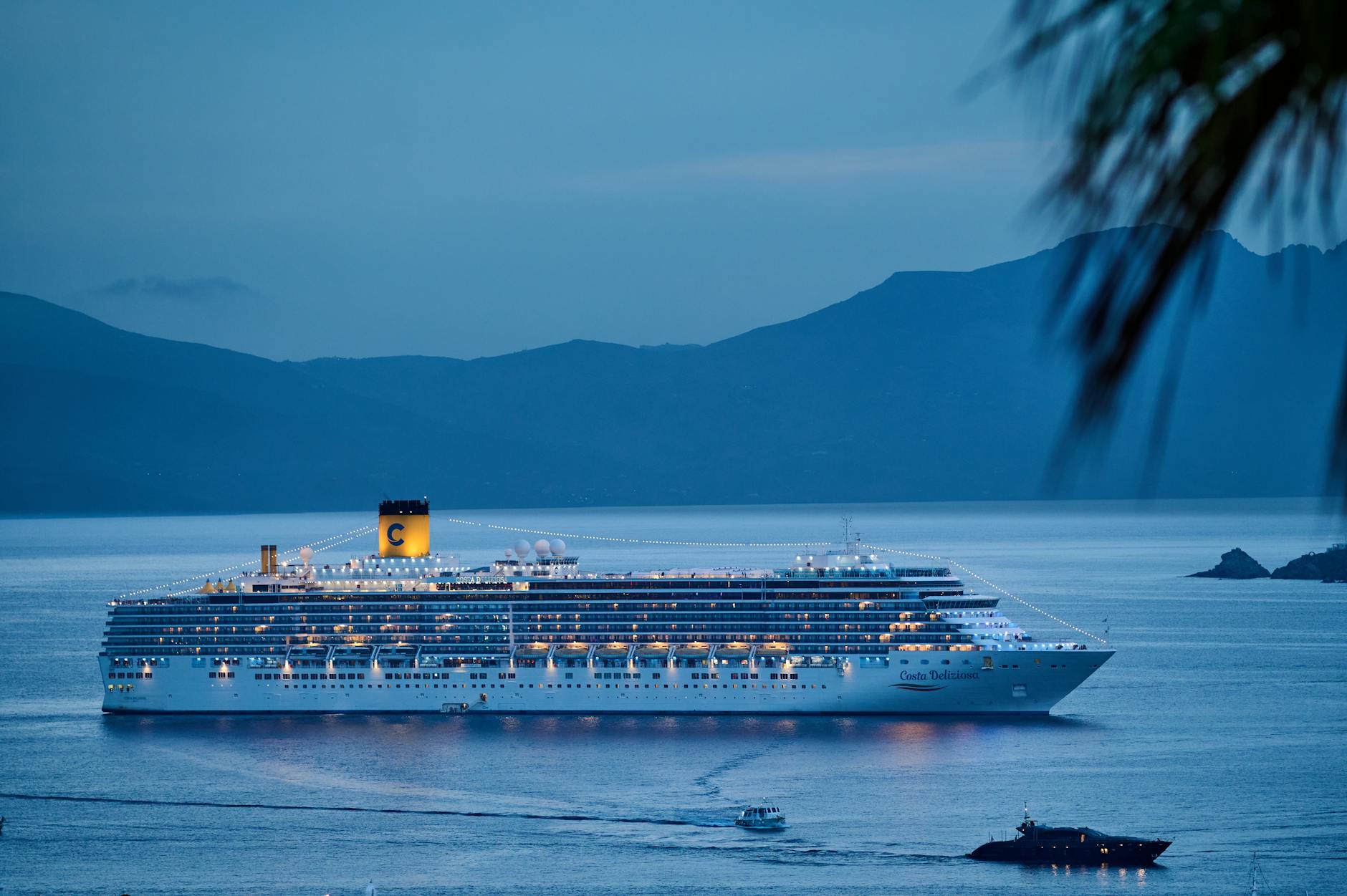 Ein beleuchtetes Kreuzfahrtschiff liegt am Abend im Meer vor einer Bergkulisse.