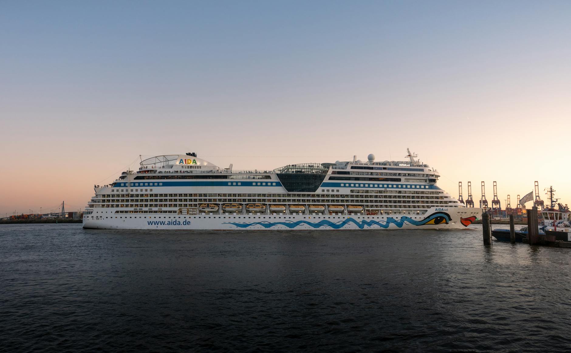 Ein großes weißes Kreuzfahrtschiff mit dem Namen AIDA und der Internetadresse www.aida.de liegt im Hafen.