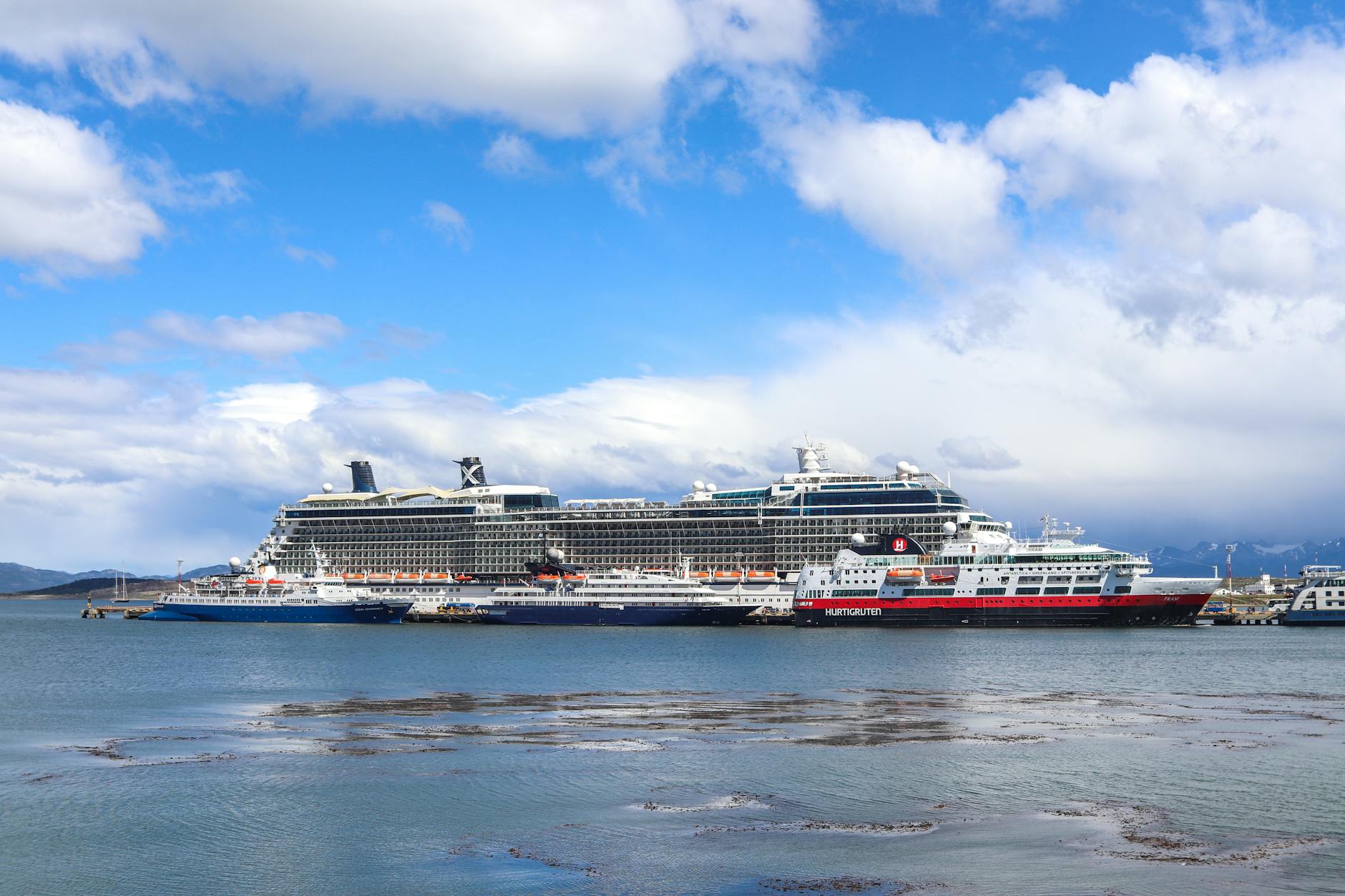 Mehrere Schiffe, darunter ein großes Kreuzfahrtschiff und ein kleineres Schiff mit der Aufschrift 