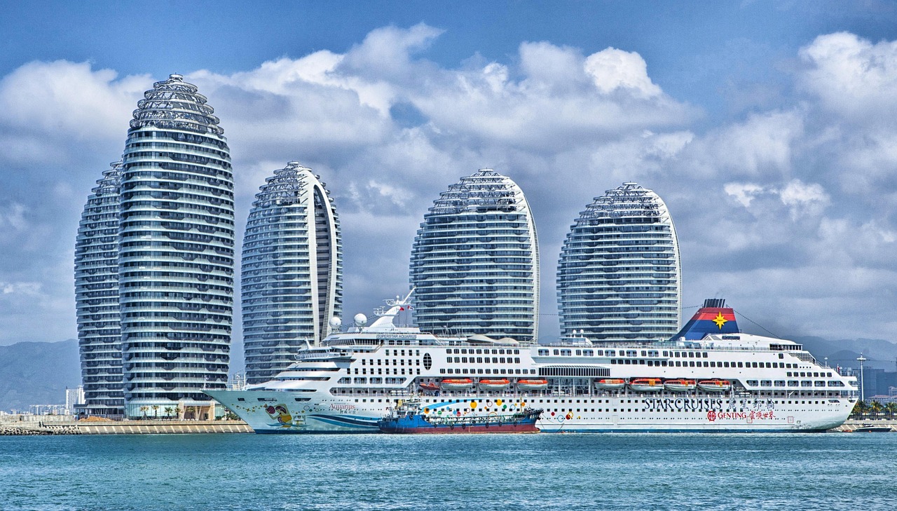 Ein großes Kreuzfahrtschiff liegt im Hafen vor einer Reihe von futuristisch aussehenden Hochhäusern.