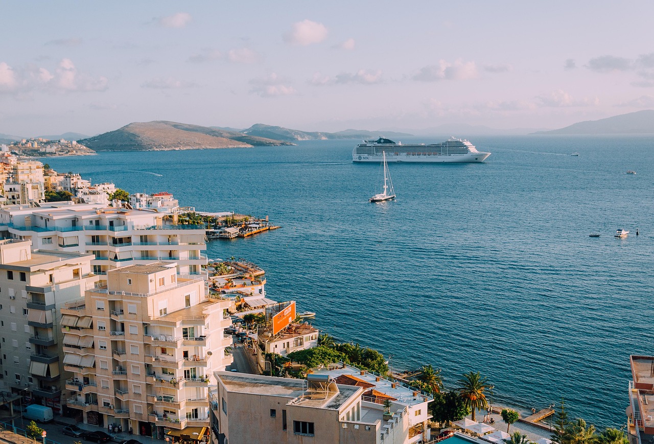 Eine Stadt am Meer mit Gebaeuden, einem Kreuzfahrtschiff und einem Segelboot auf dem Wasser.