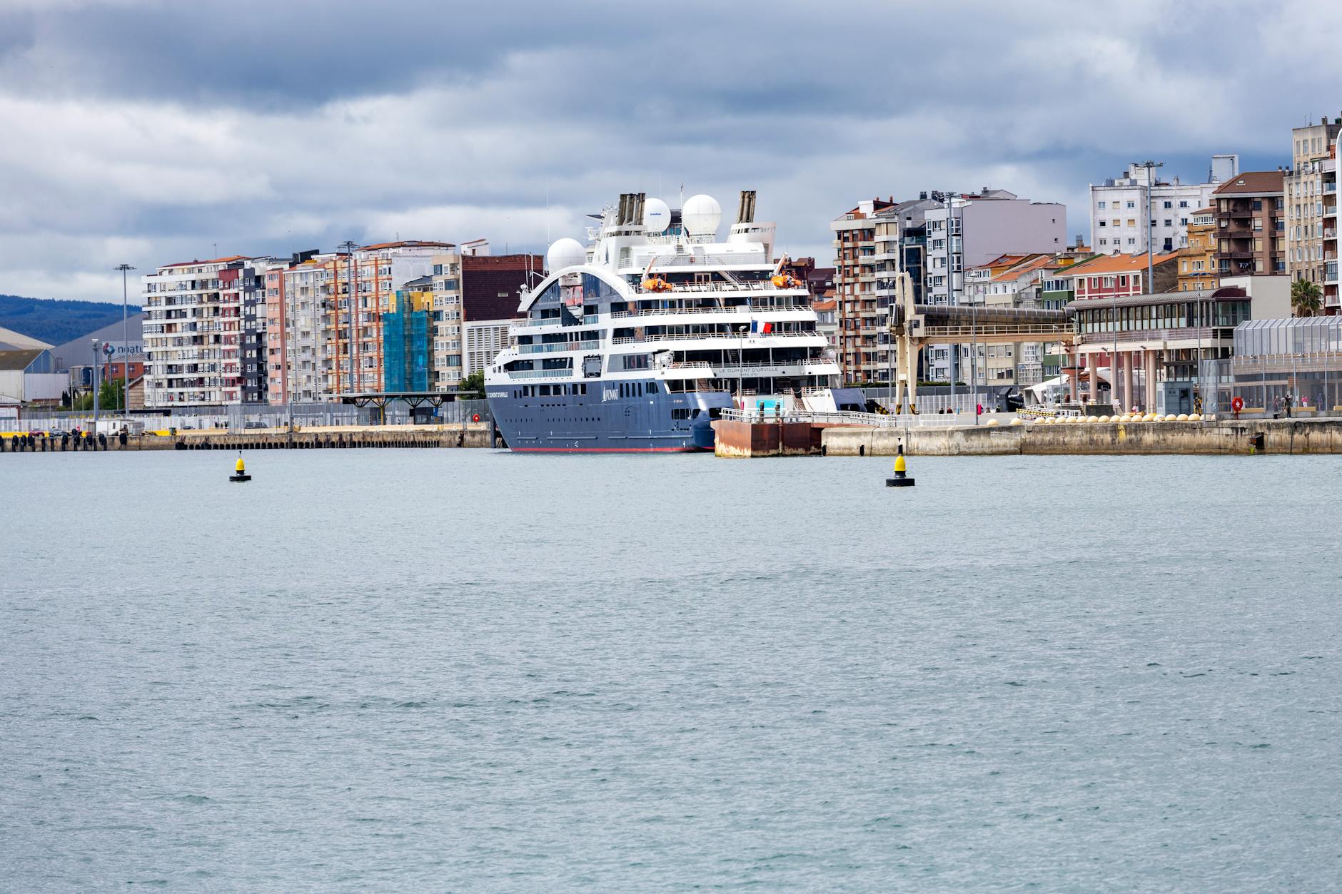 Ponant Kreuzfahrtschiff - Large cruise ship docked at a city port with a scenic urban backdrop on a cloudy