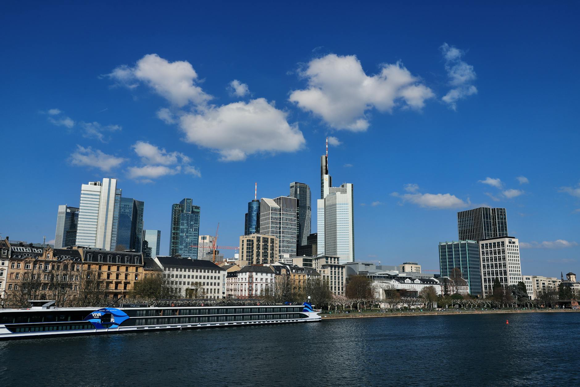Die Skyline von Frankfurt am Main mit modernen Hochhäusern und einem Flusskreuzfahrtschiff auf dem Main.