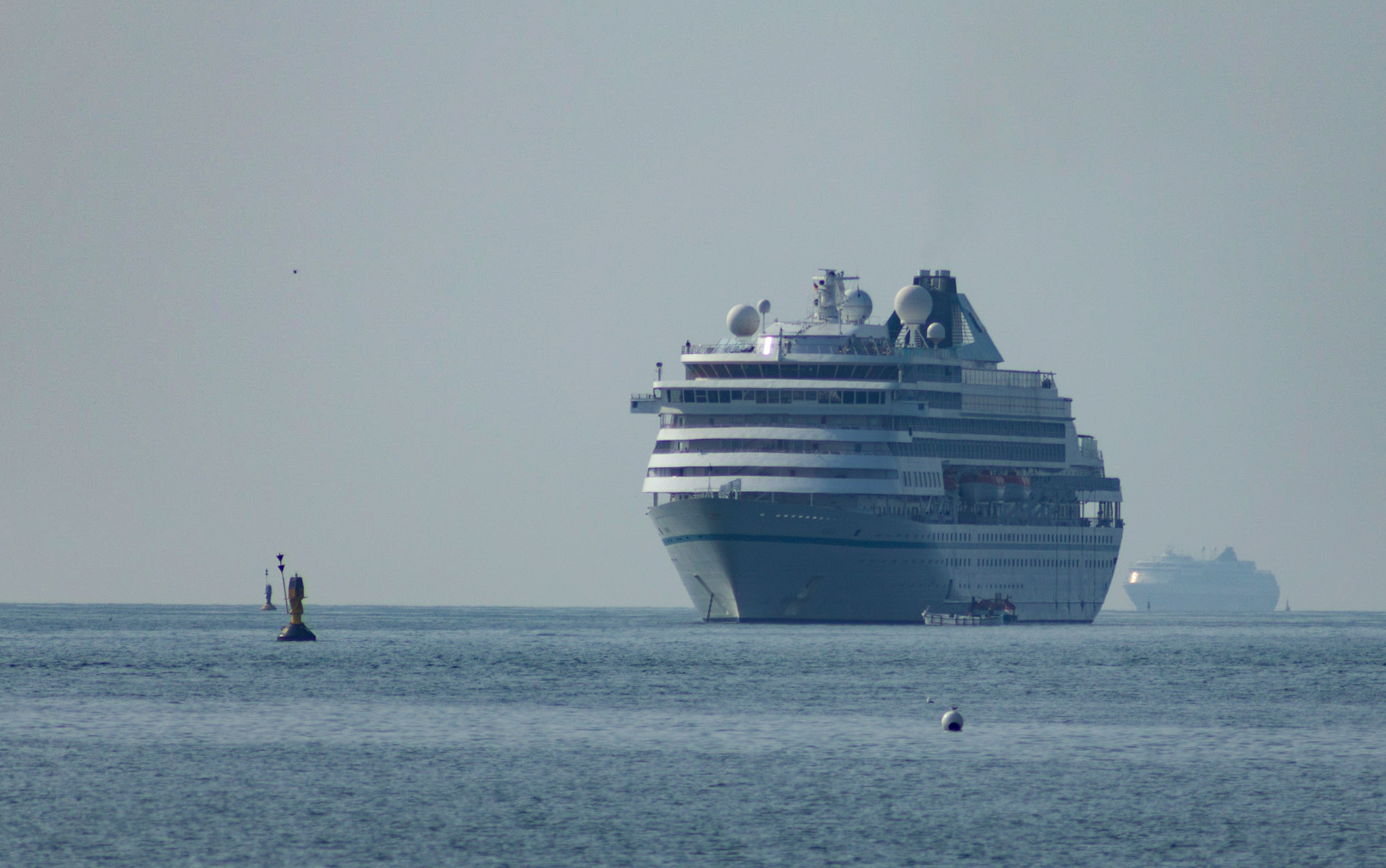 Ein großes Kreuzfahrtschiff fährt auf dem Meer, im Hintergrund ist ein weiteres Schiff zu sehen.