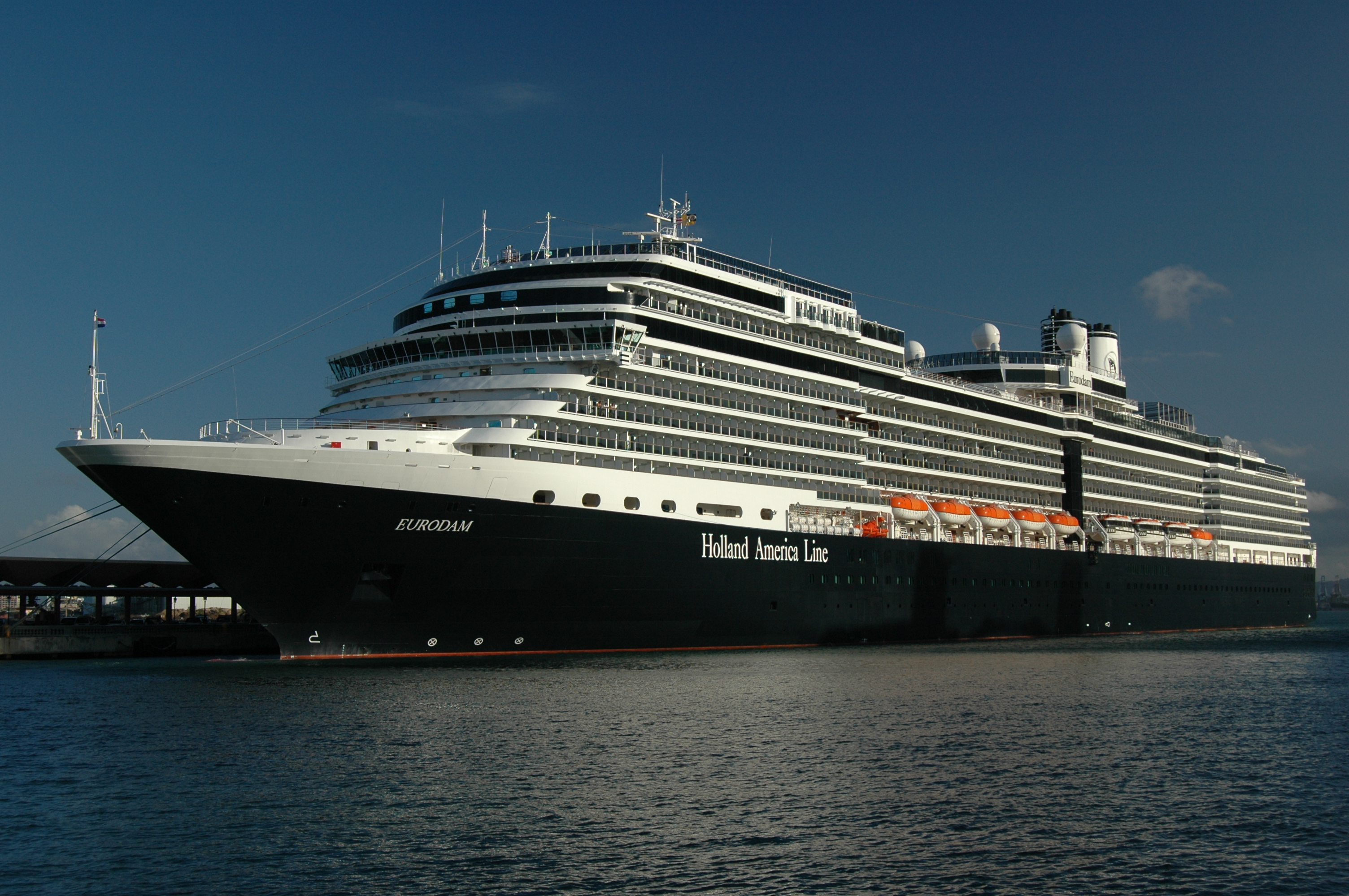 Ein großes schwarzes Kreuzfahrtschiff namens Eurodam der Holland America Line liegt im Hafen vor einer blauen Kulisse.