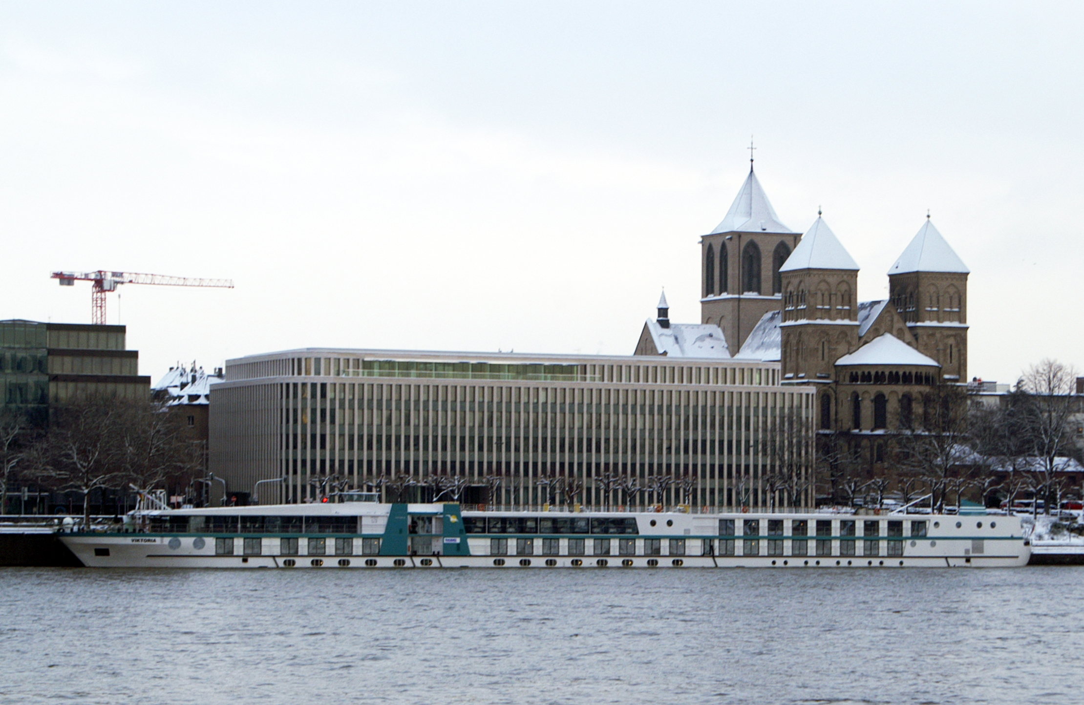 Ein weisses Flussschiff liegt im Wasser vor einer Stadtkulisse mit einer Kirche und modernen Gebaeuden.