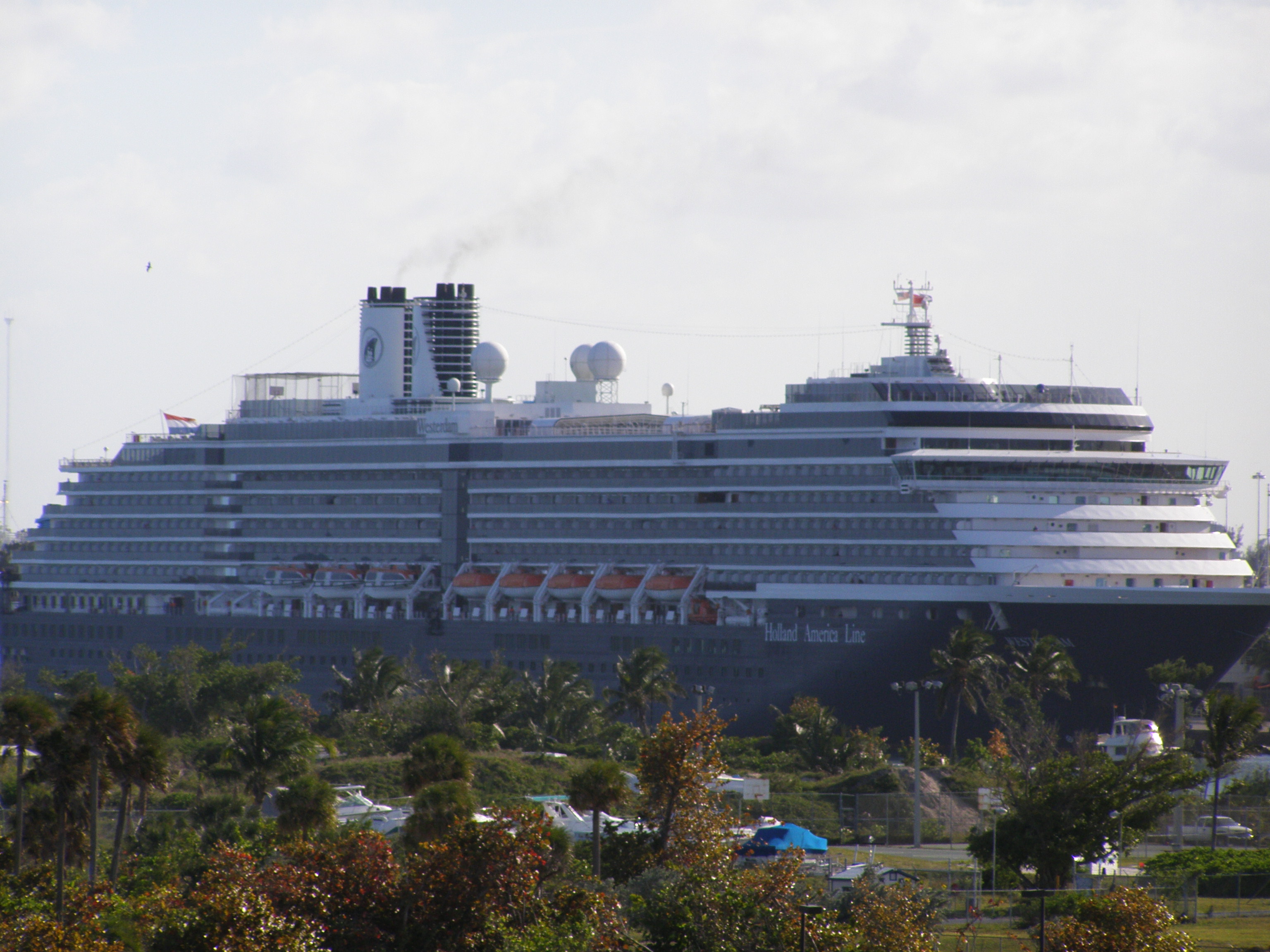 Ein großes Kreuzfahrtschiff der Holland America Line mit dem Namen Westerdam liegt vor Anker, mit Rauch aus den Schornsteinen und Rettungsbooten an der Seite.