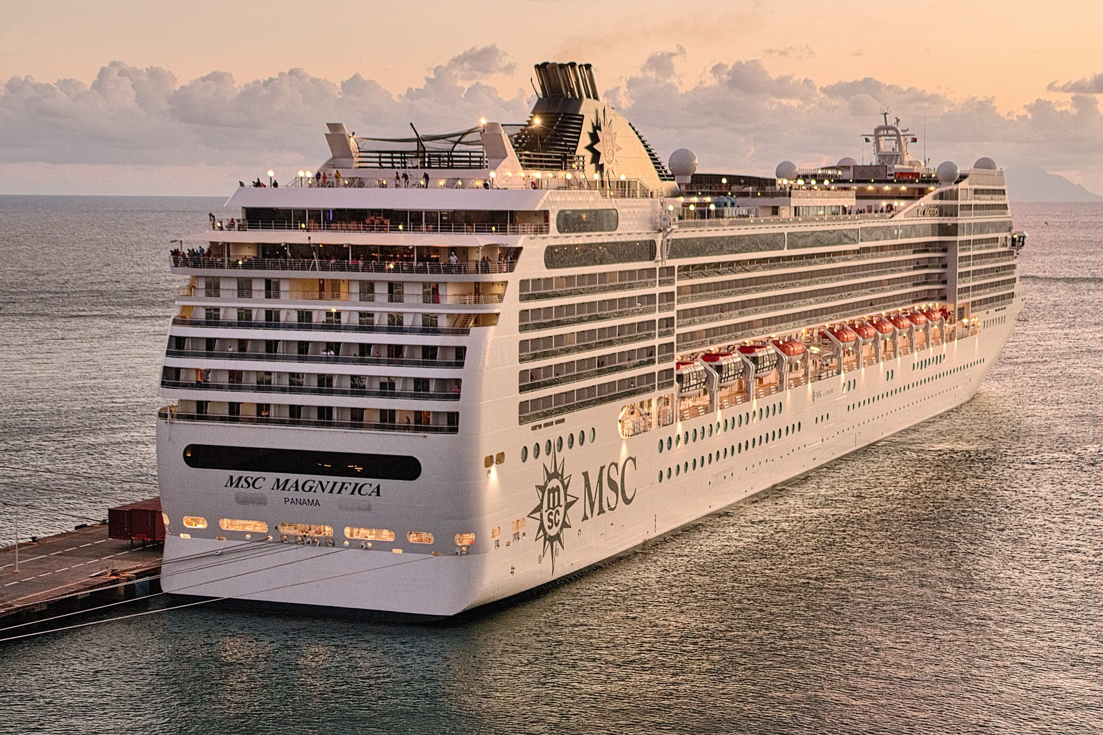 Ein großes weißes Kreuzfahrtschiff mit dem Namen MSC Magnifica liegt im Hafen, während die Sonne untergeht.