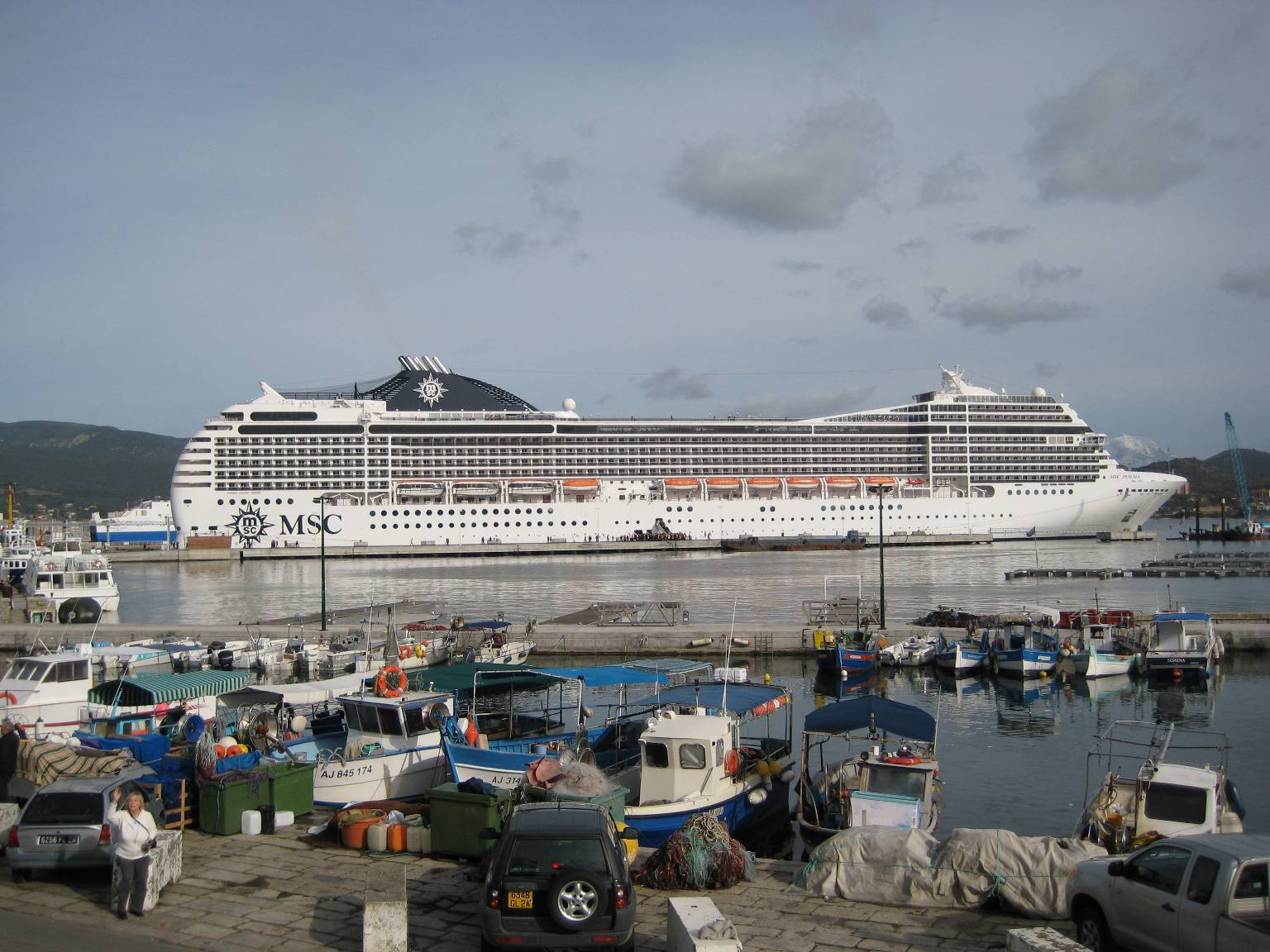 Ein großes weißes Kreuzfahrtschiff liegt im Hafen neben kleineren Fischerbooten.
