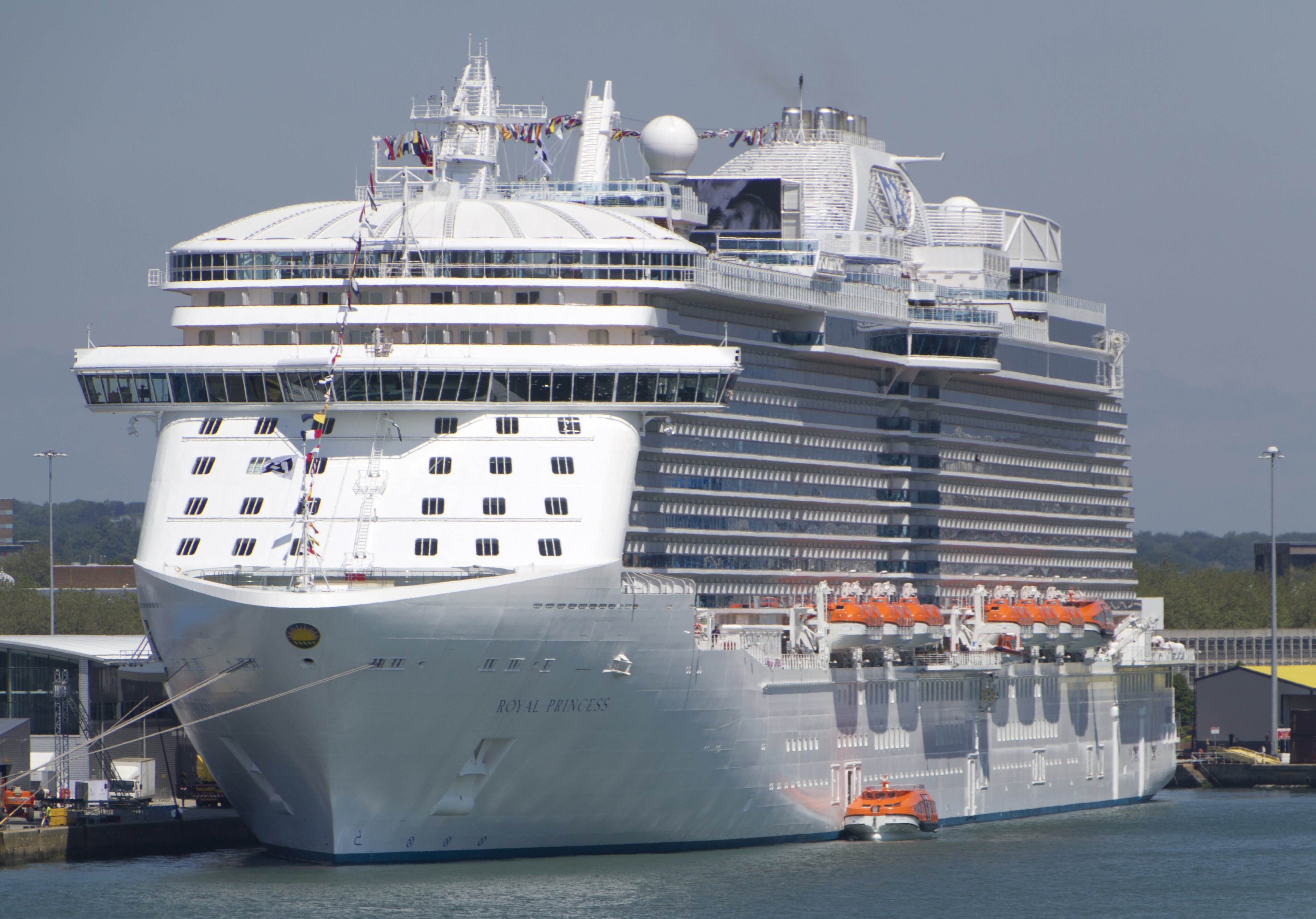 Ein großes weißes Kreuzfahrtschiff namens Royal Princess liegt im Hafen, mit vielen Rettungsbooten an der Seite.