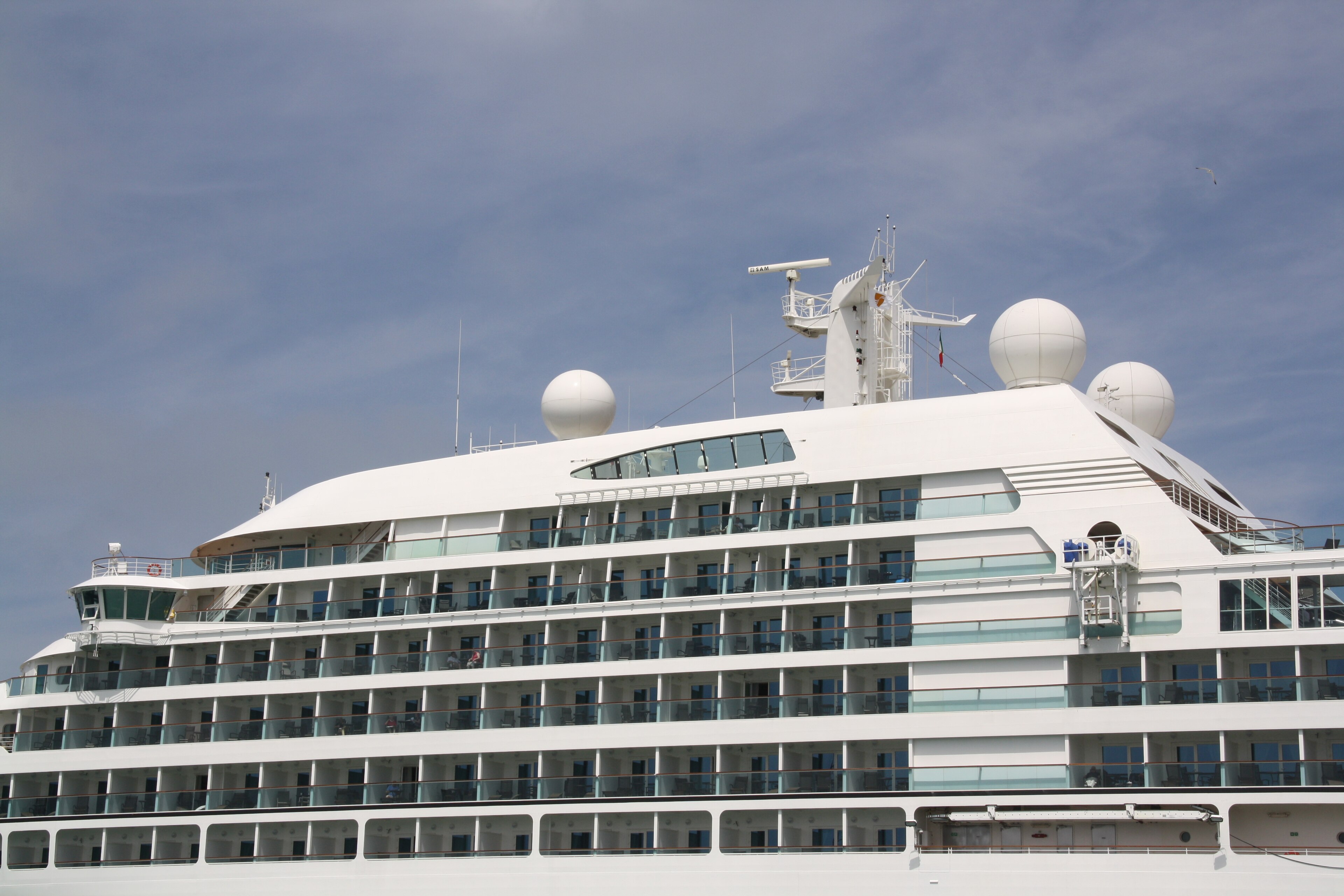 Ein grosses weisses Kreuzfahrtschiff mit vielen Balkonen und Fenstern liegt im Hafen.