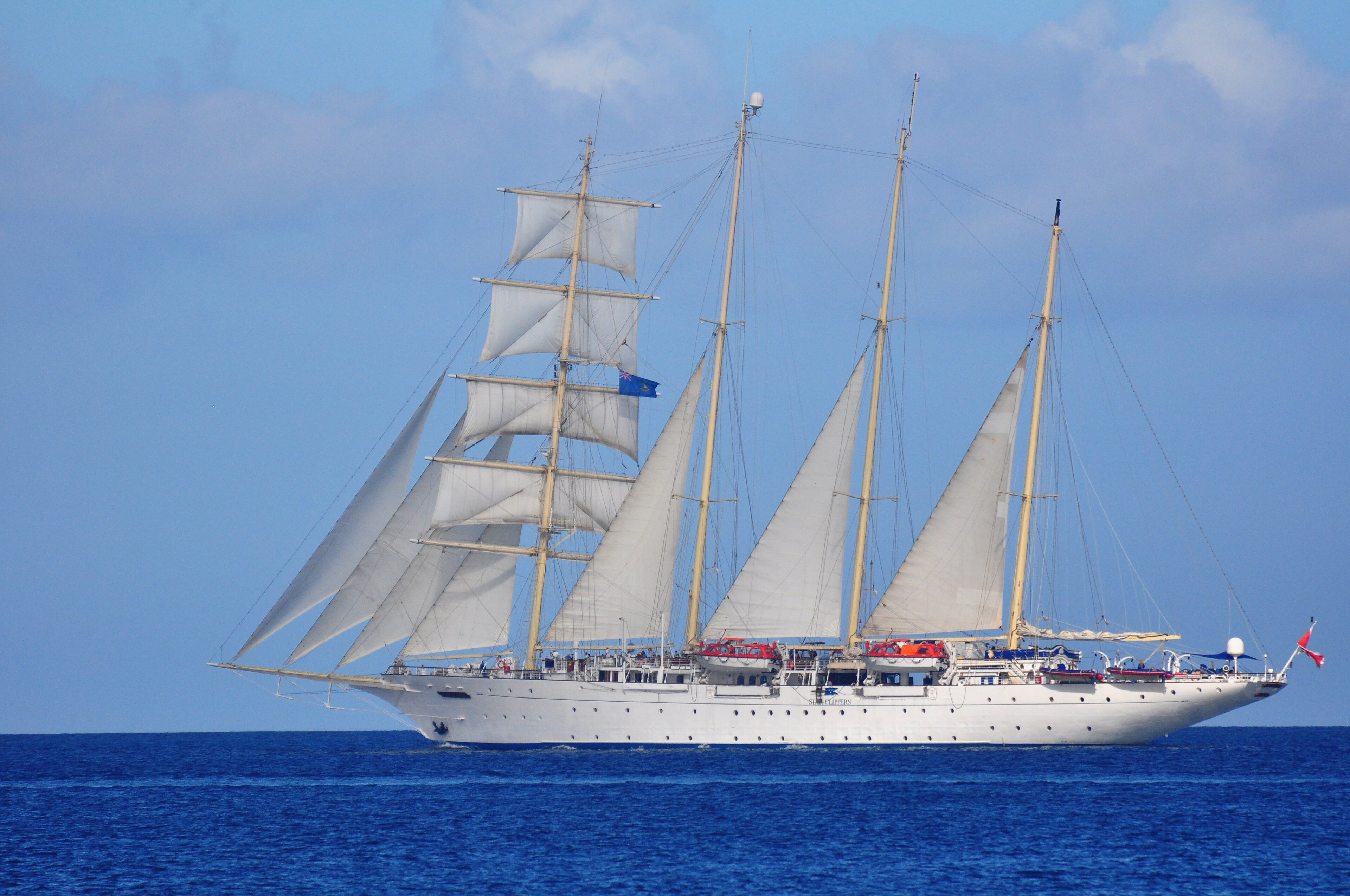 Ein großes weißes Segelschiff mit vier Masten und weißen Segeln fährt auf dem blauen Meer.