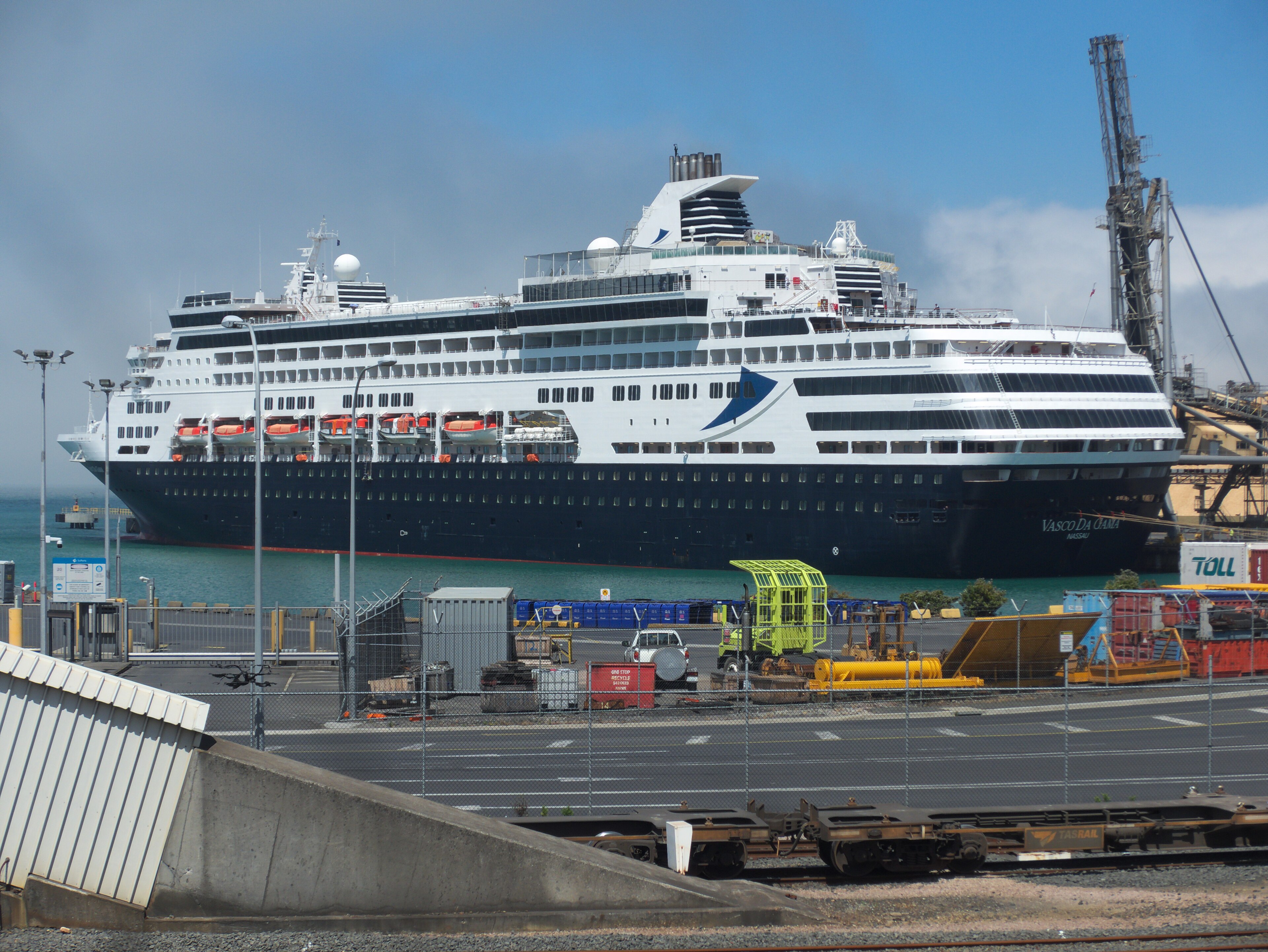 Ein großes Kreuzfahrtschiff mit dem Namen Vasco da Gama liegt im Hafen neben einem Kran und Containern.