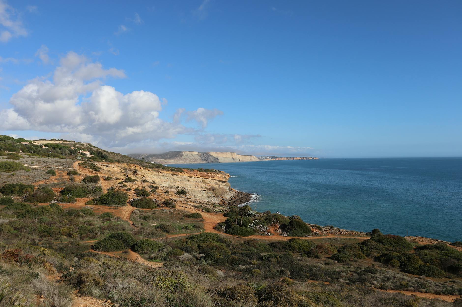 Algarve, Portugal - Eine felsige Kueste mit gruener Vegetation und dem blauen Meer unter einem Himmel mit Wolken.